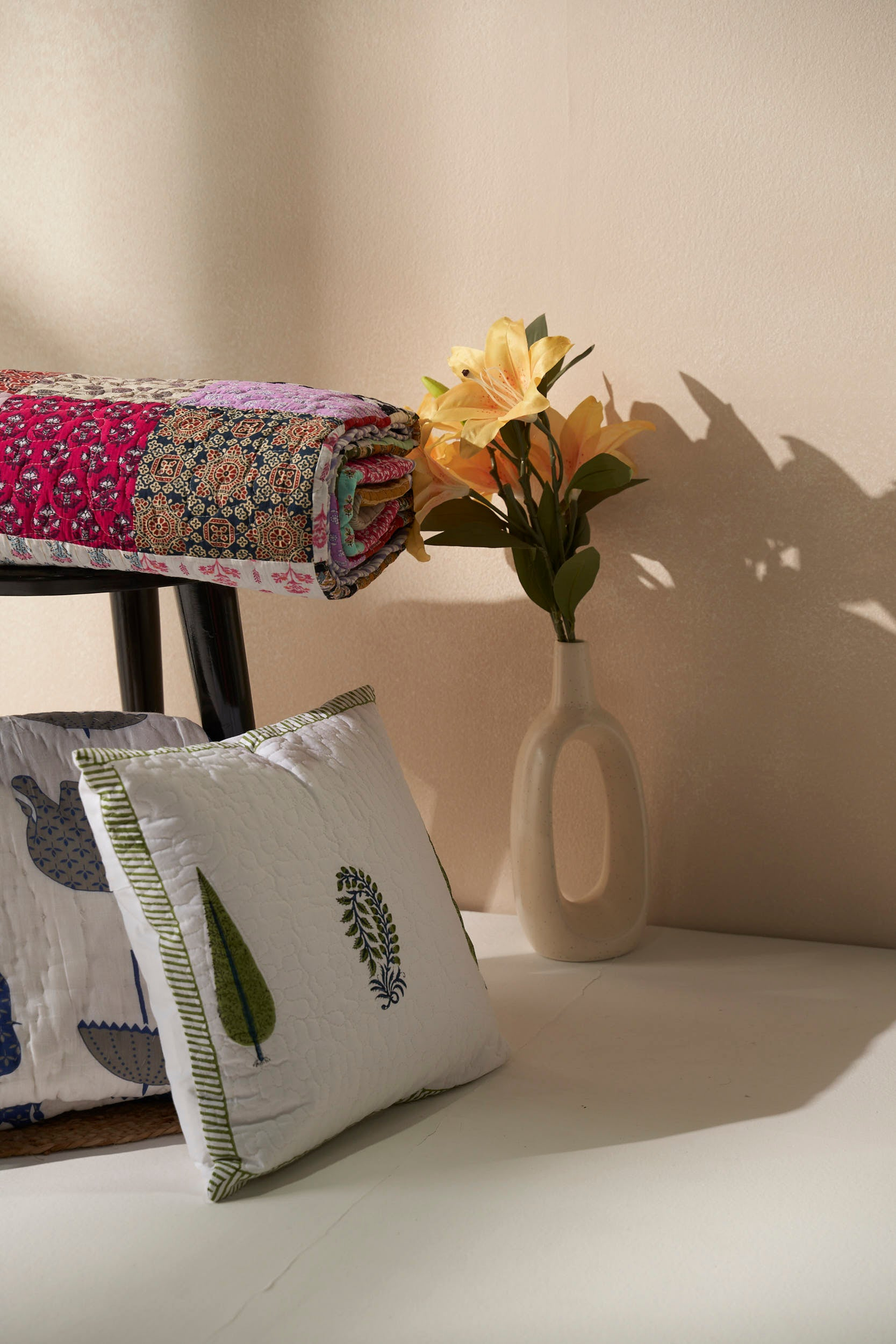 Artisanal cotton quilt and block-printed cushion set styled with fresh florals — soft, slow-living accents for soulful homes.