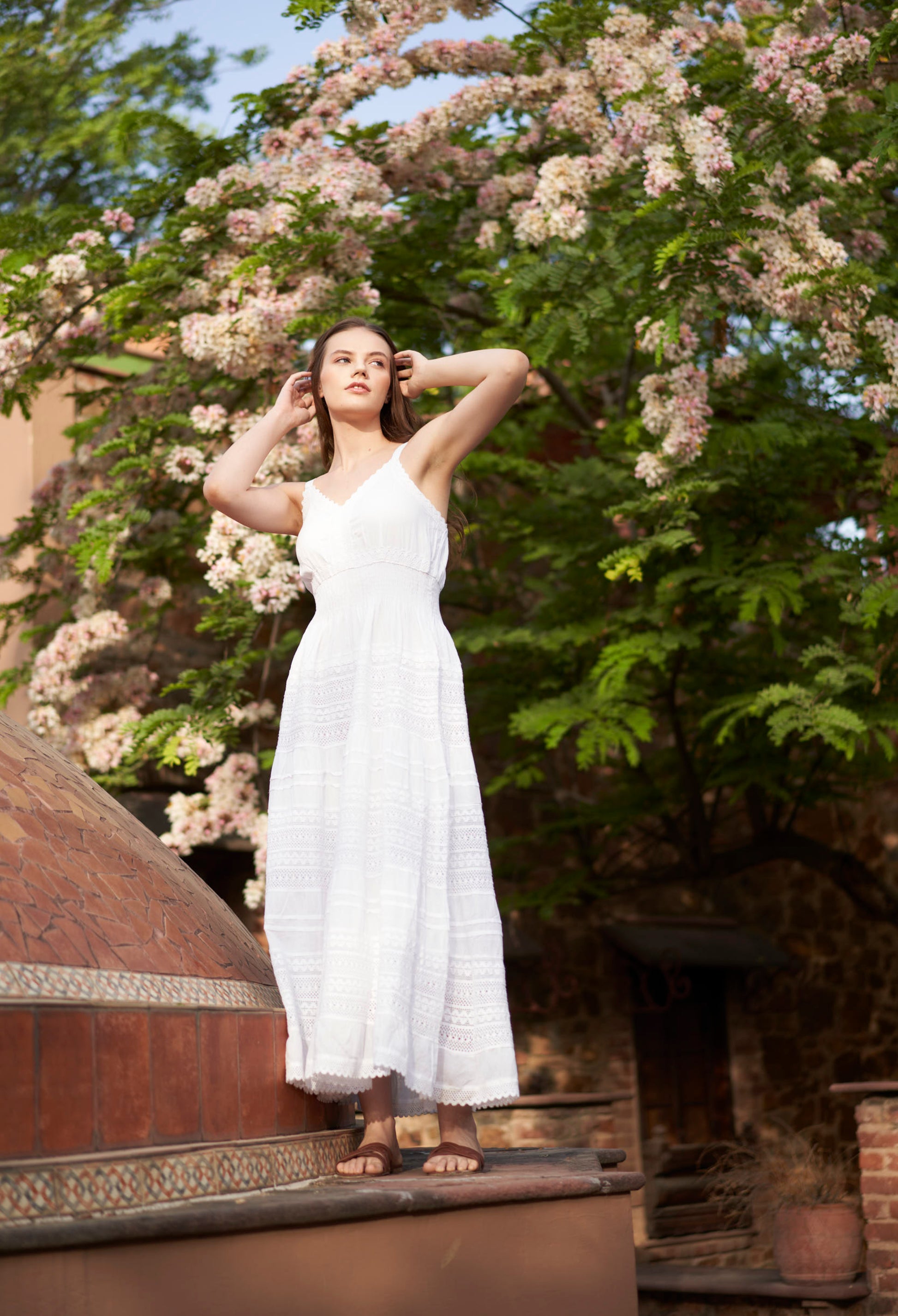 Woman in a white dress standing outdoors with greenery and a building in the background