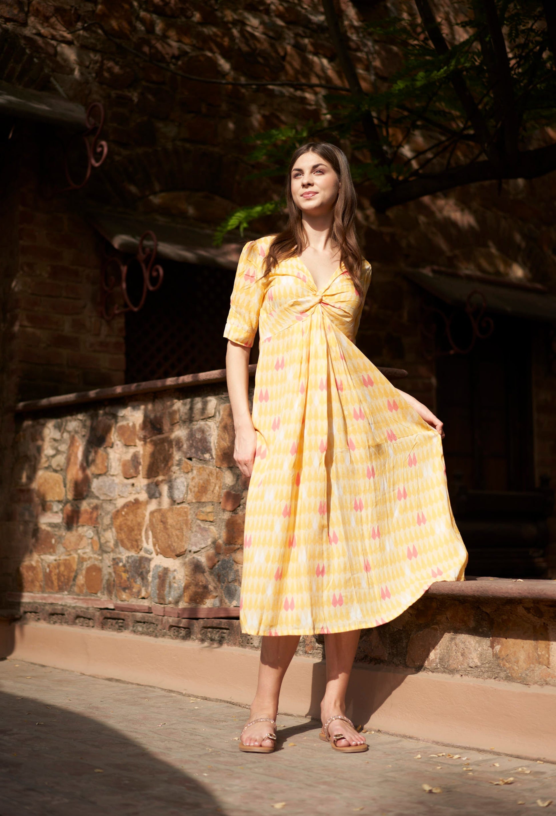 Woman in a yellow dress standing in front of a stone wall.