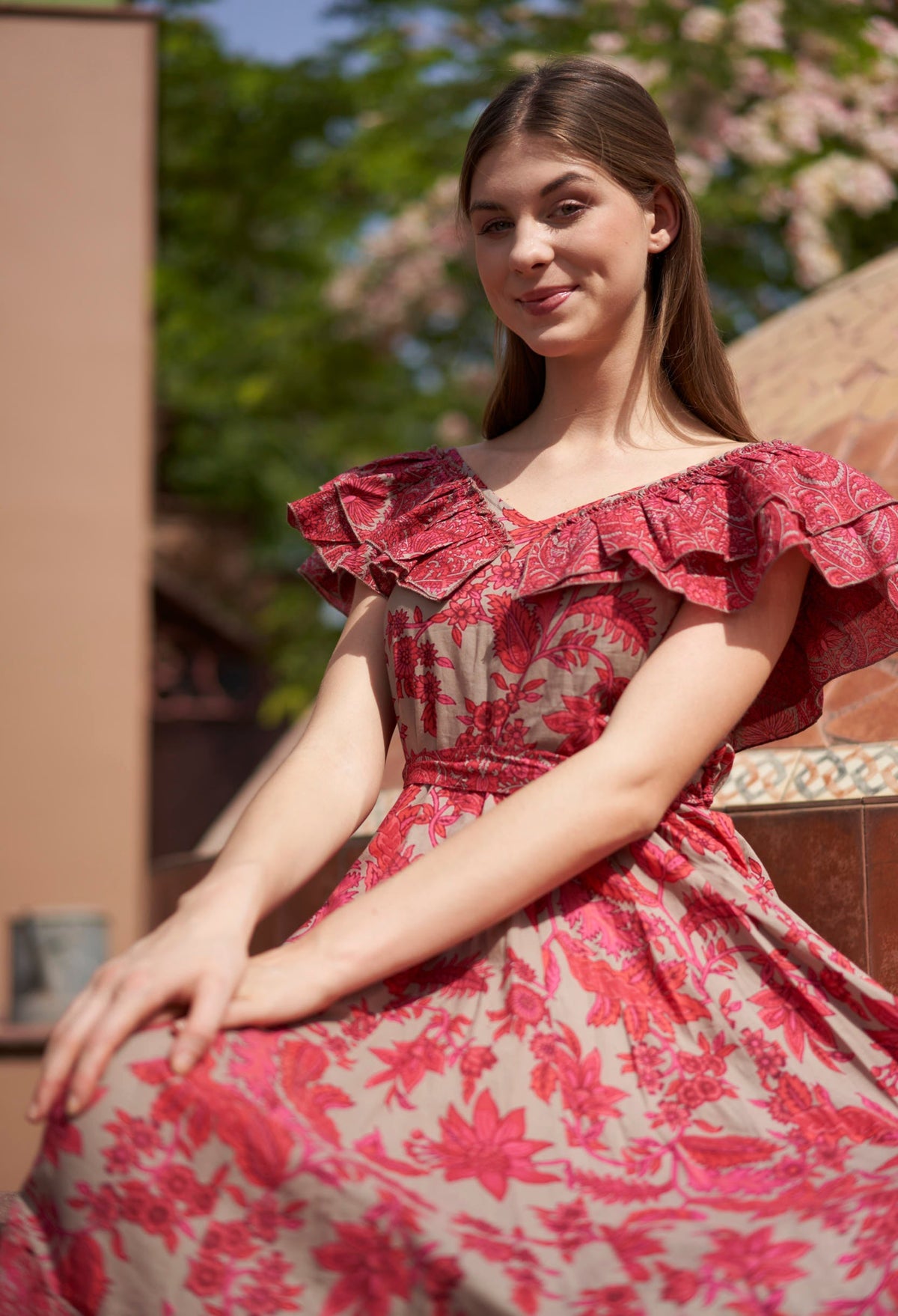 Woman wearing a red floral dress sitting outdoors with trees in the background