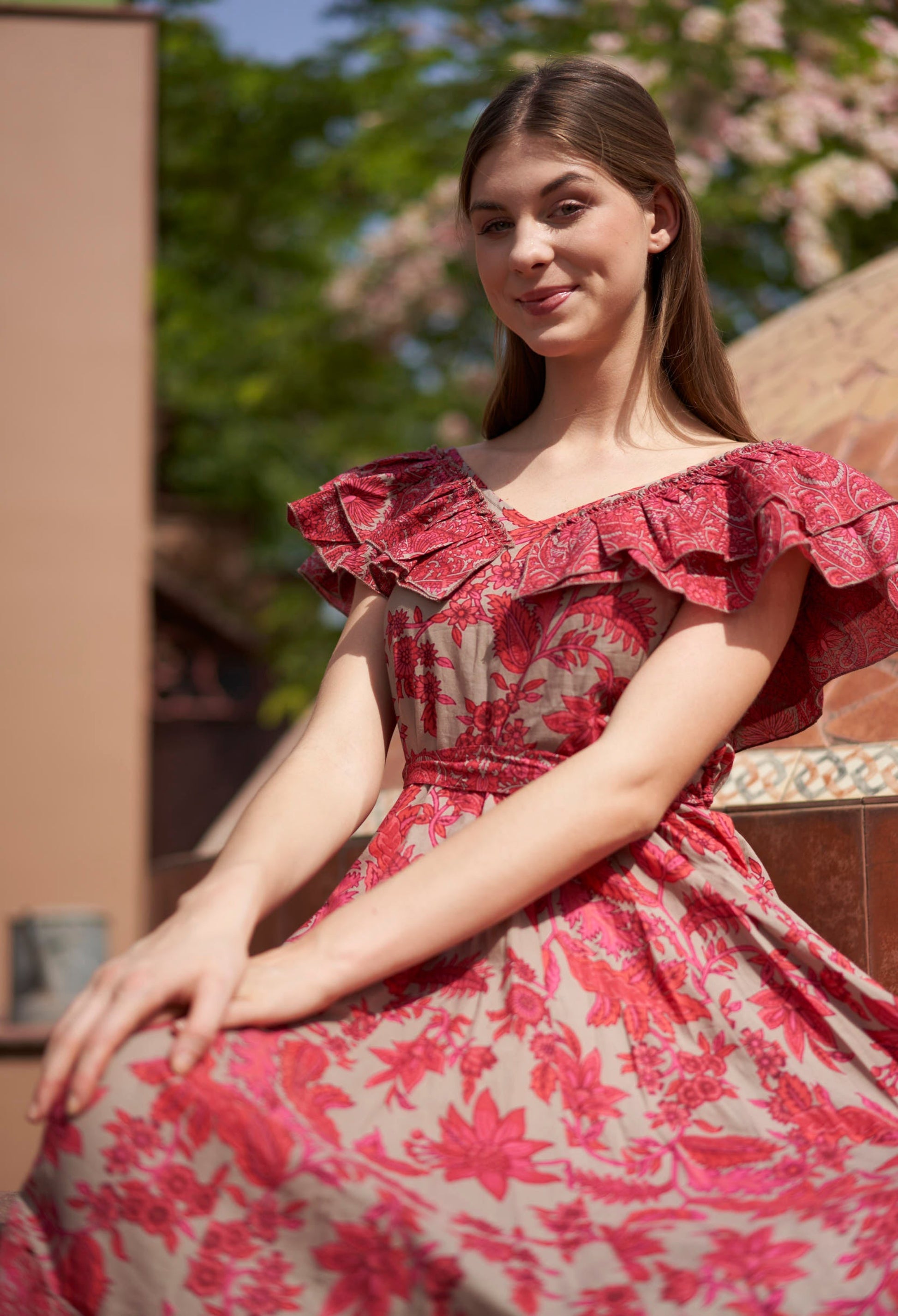 Woman wearing a red floral dress sitting outdoors with trees in the background