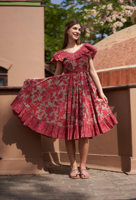 Woman wearing a red floral dress standing outdoors with a building and trees in the background