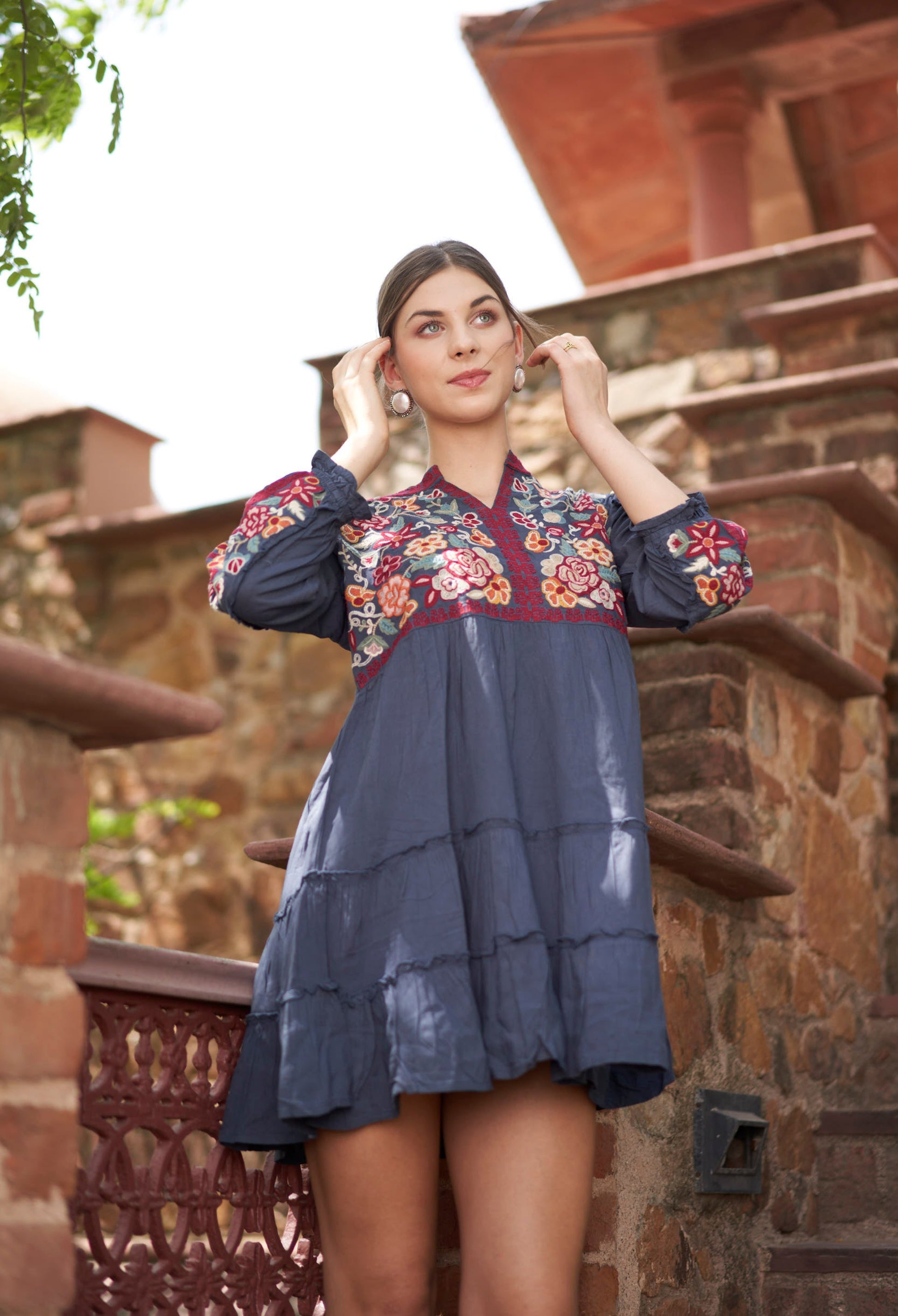 Woman wearing a floral embroidered dress standing outdoors with stone architecture in the background
