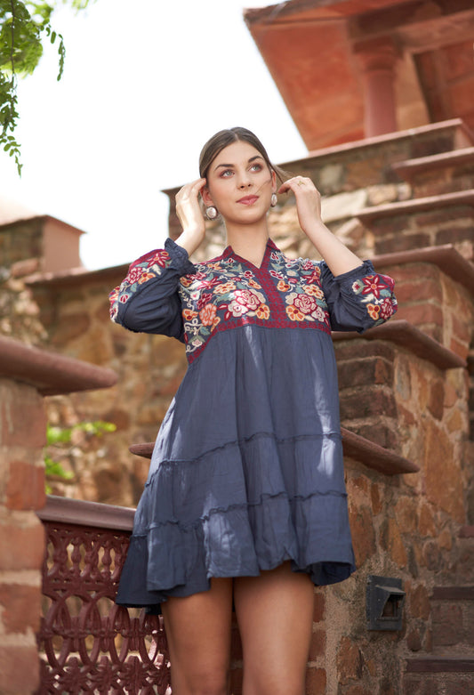 Woman wearing a floral embroidered dress standing outdoors with stone architecture in the background