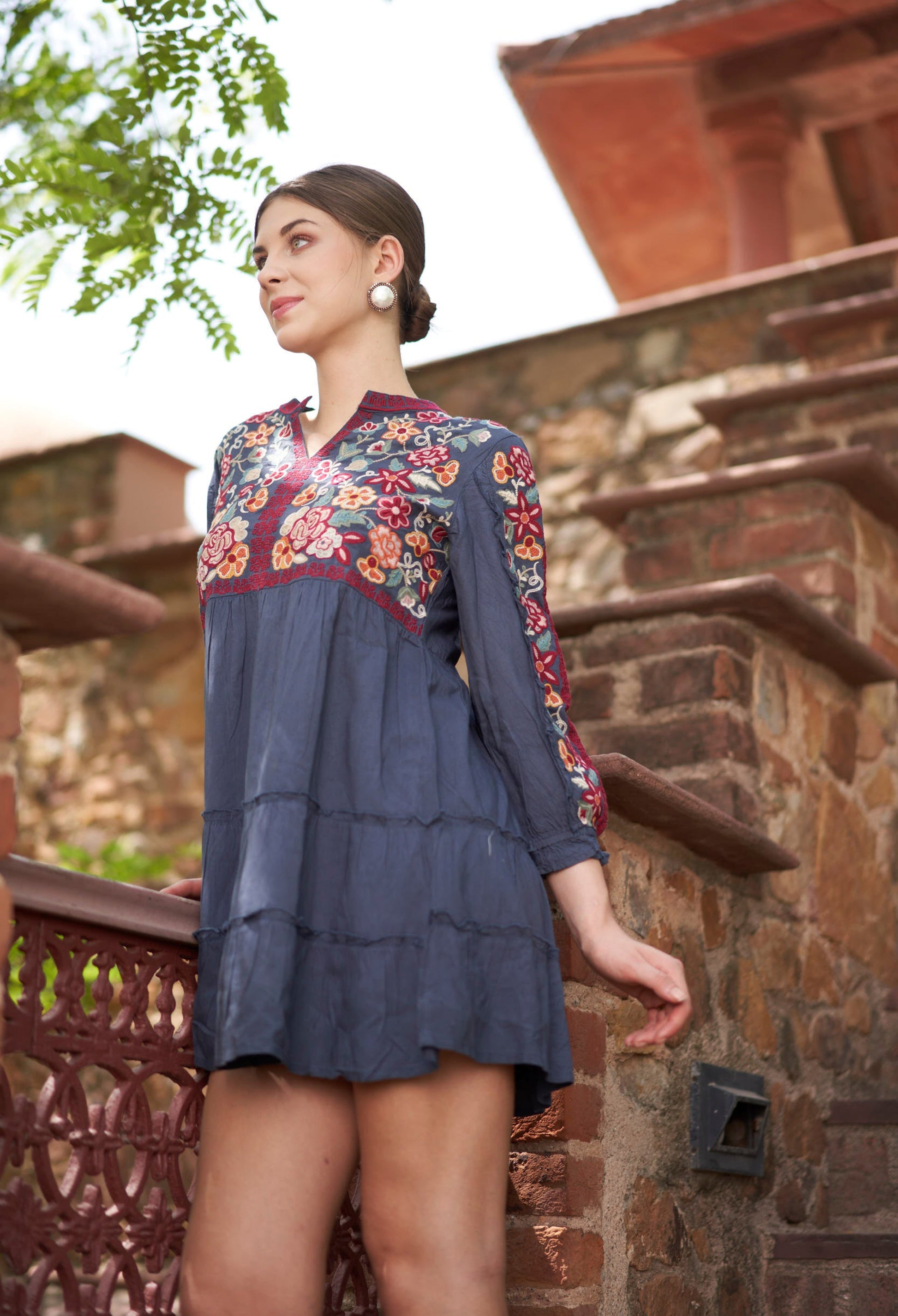 Woman wearing a blue dress with floral embroidery standing on a stone staircase.