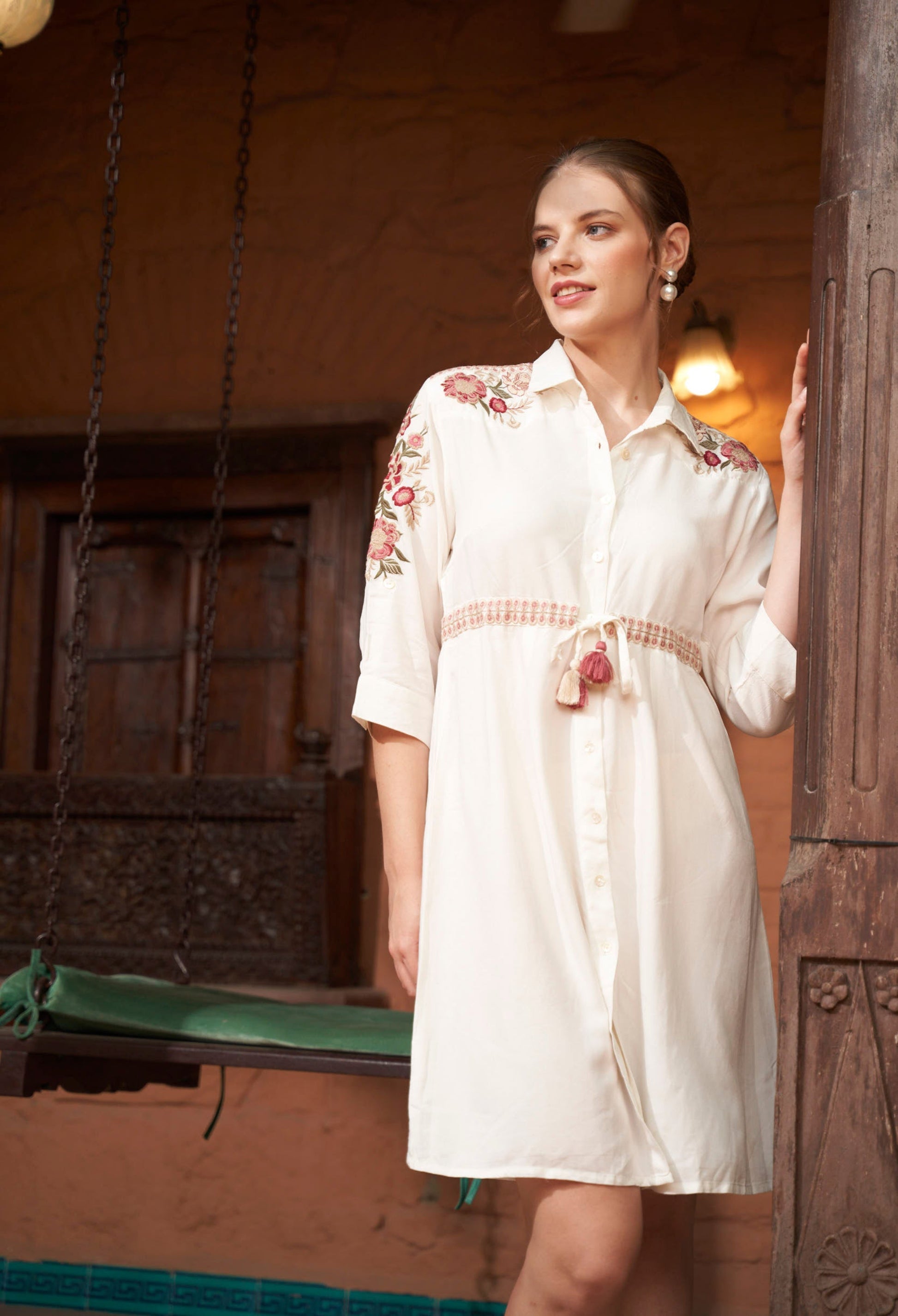 Woman wearing a white dress with floral embroidery in an indoor setting