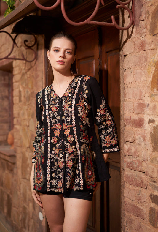 Woman wearing a black floral blouse standing in front of a rustic stone building.
