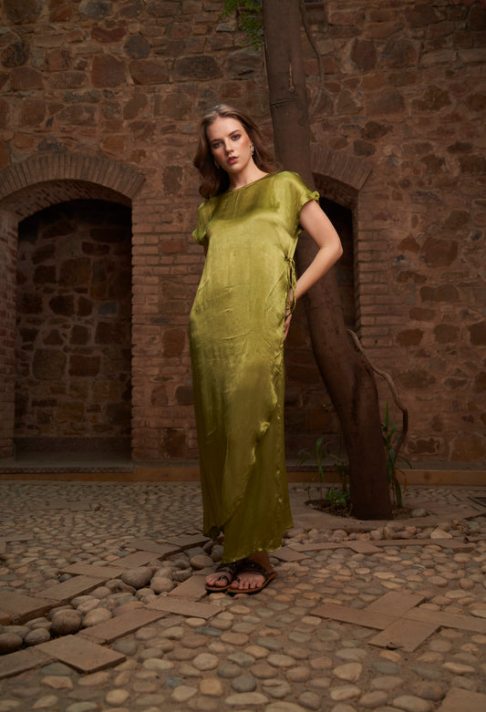 Woman in a green dress standing in front of a stone wall.