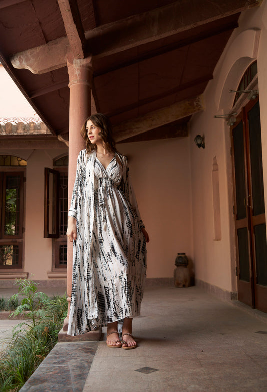 Woman in a patterned dress standing on a stone path in front of a building with a garden.