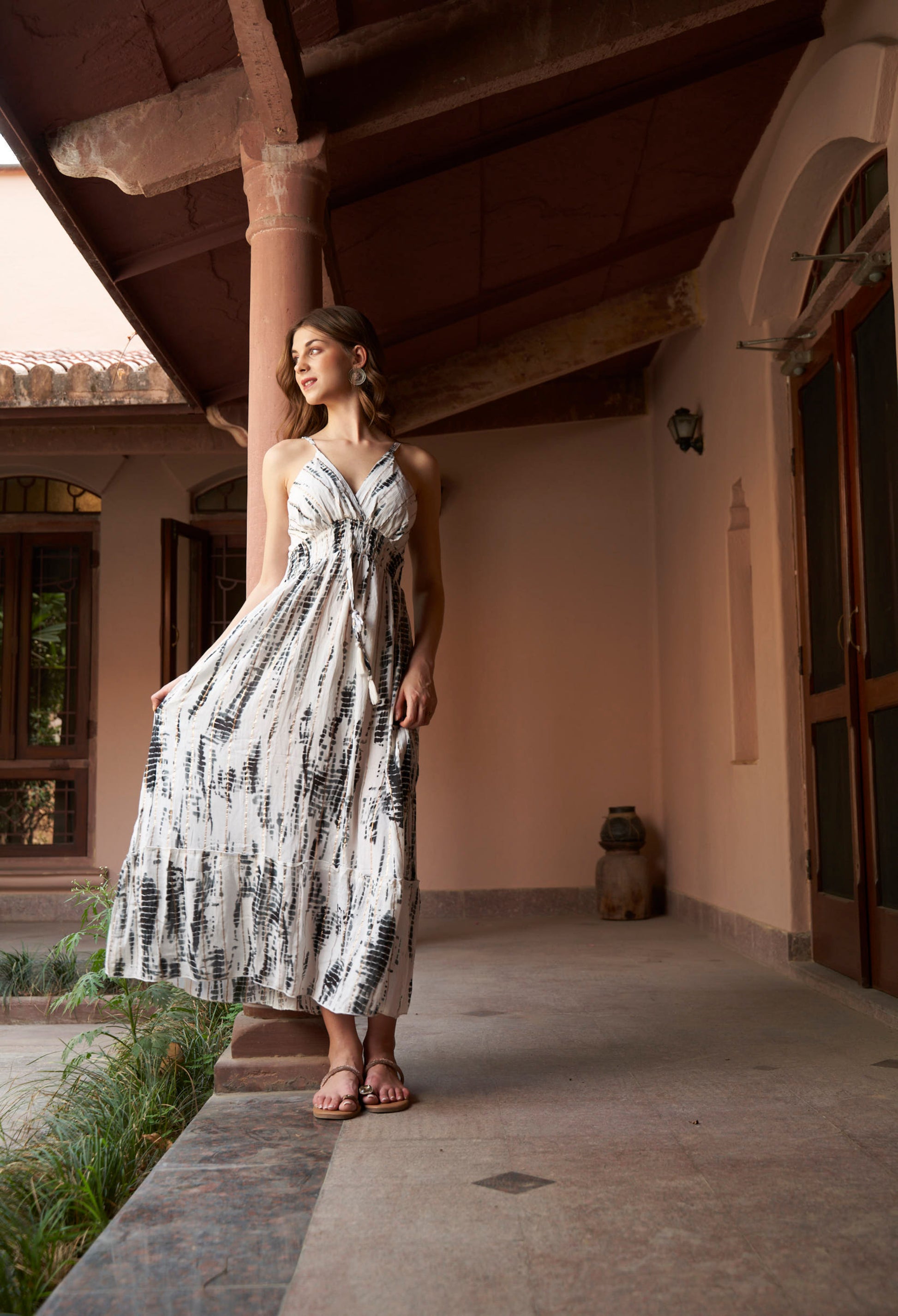 Woman in a white dress with black patterns standing on a patio.