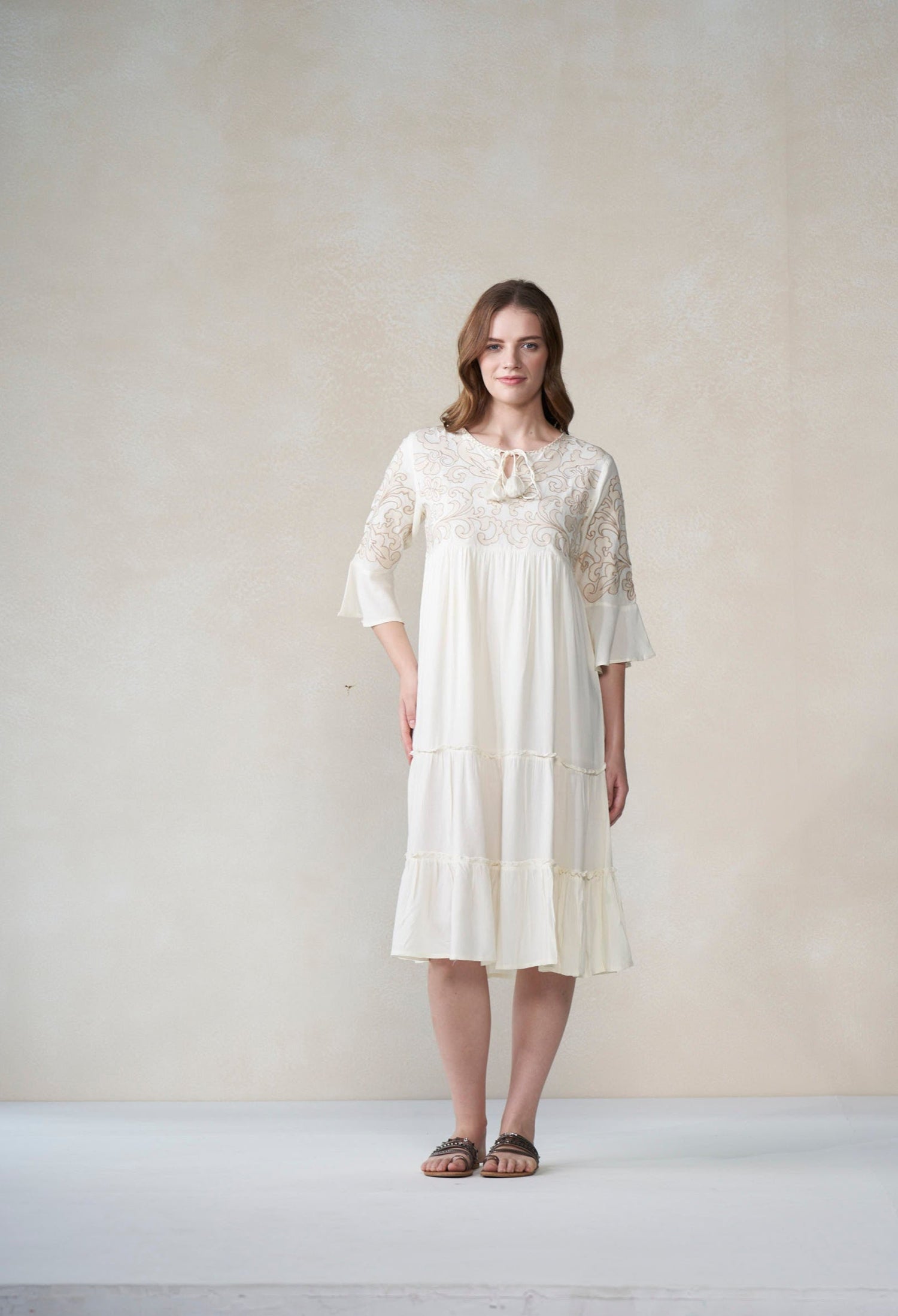 Woman wearing a ivory lace dress against a plain background