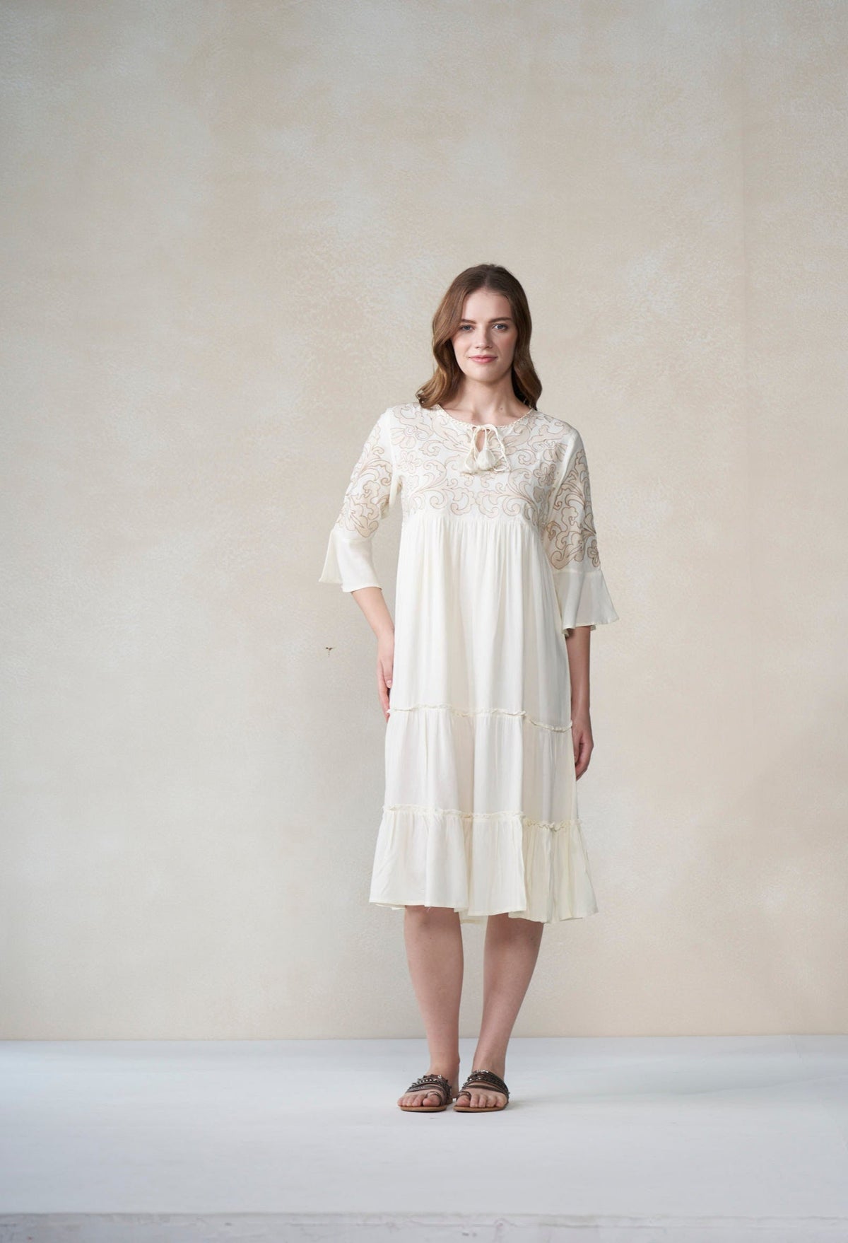 Woman wearing a ivory lace dress against a plain background