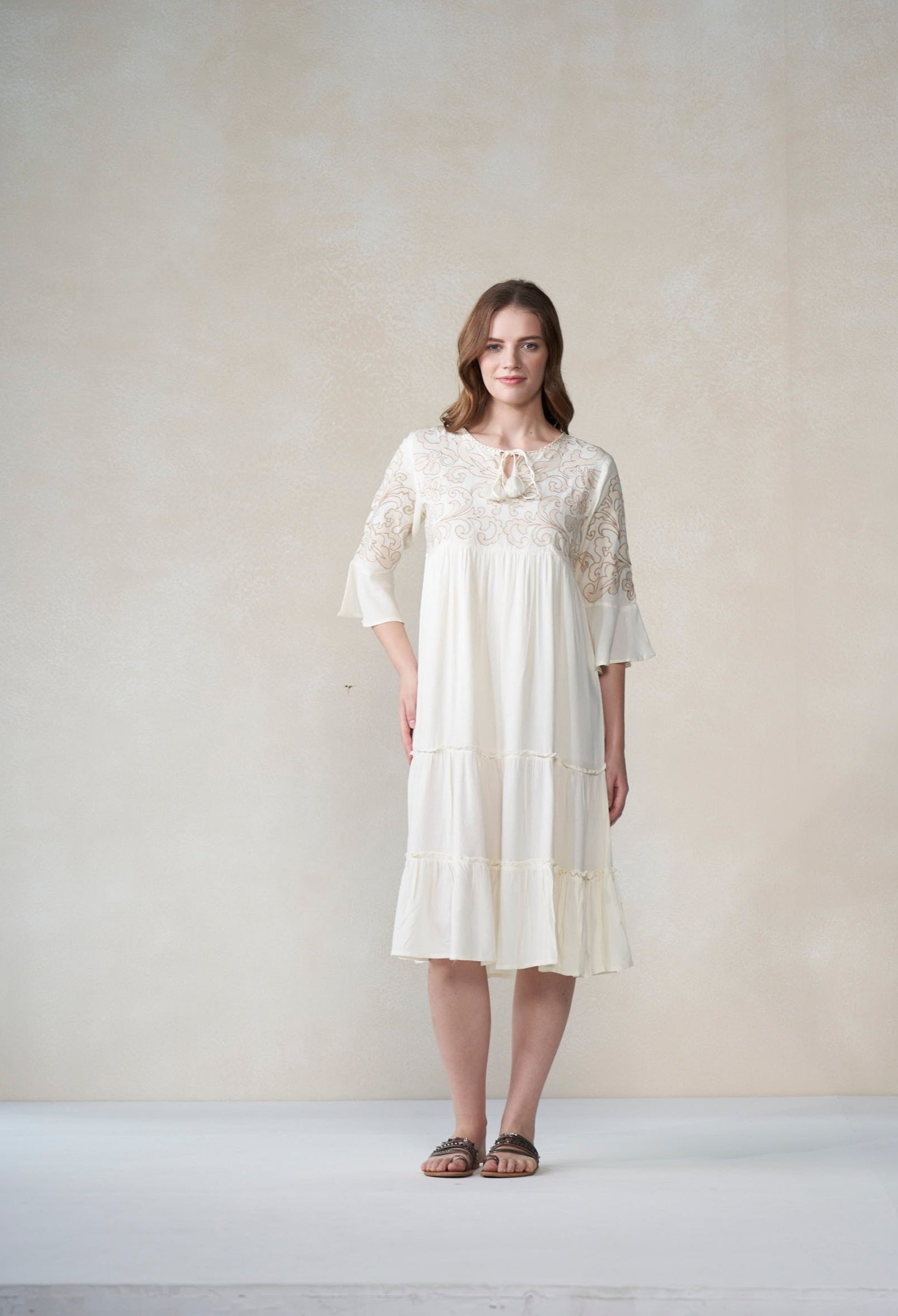 Woman wearing a ivory lace dress against a plain background