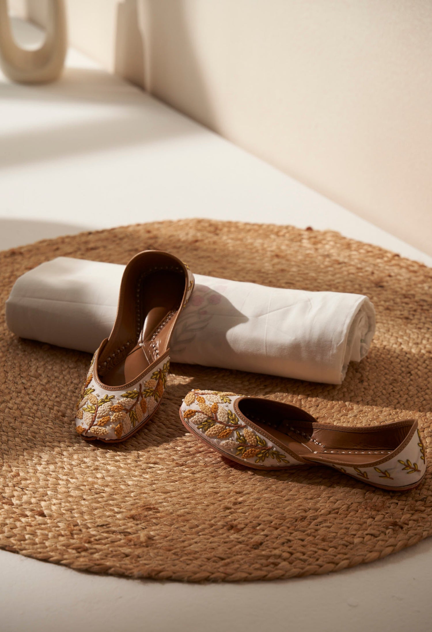 Pair of decorative white and yellow  royal indian shoes called juttis on a woven mat with a white dohar