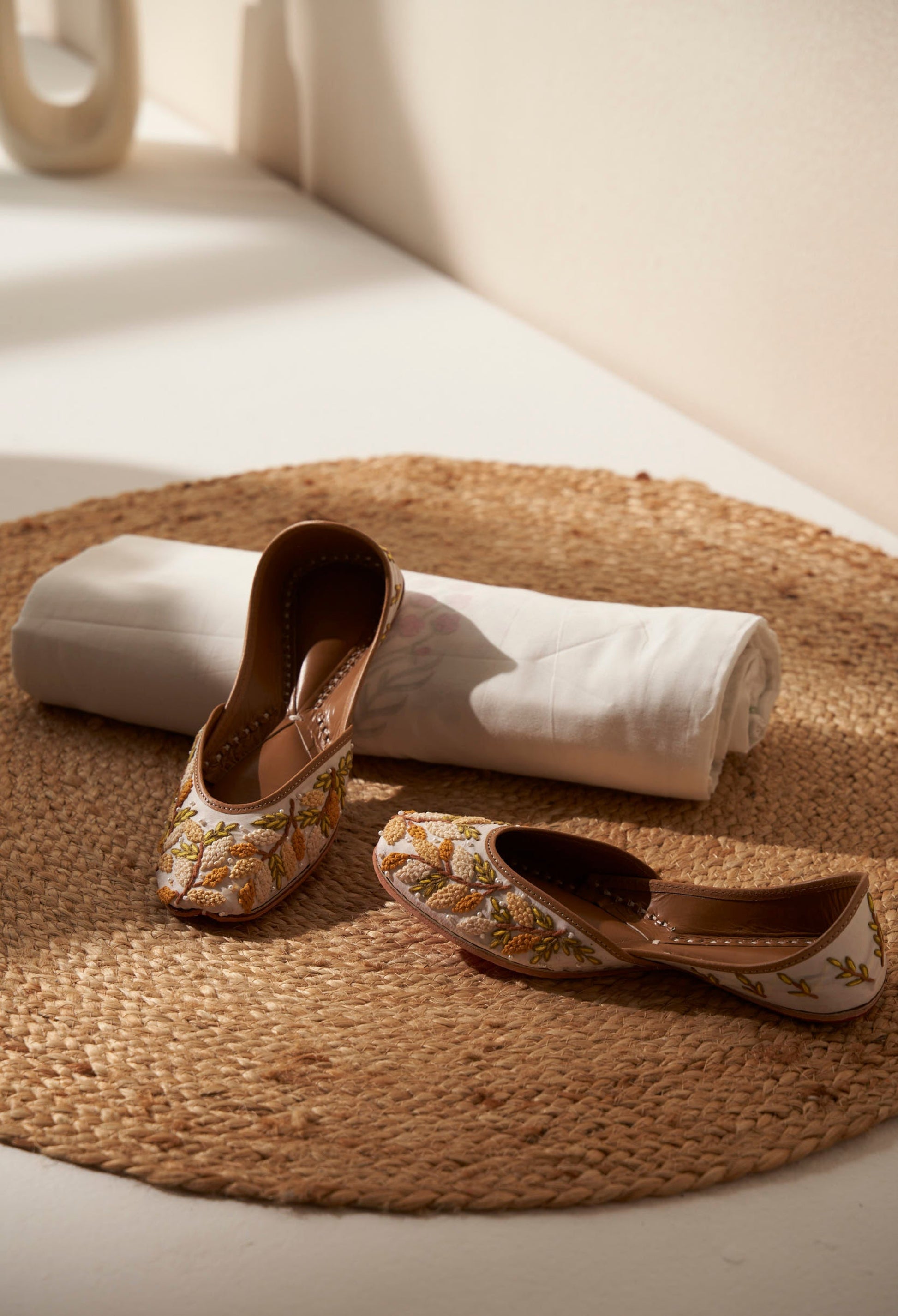 Pair of decorative white and yellow  royal indian shoes called juttis on a woven mat with a white dohar