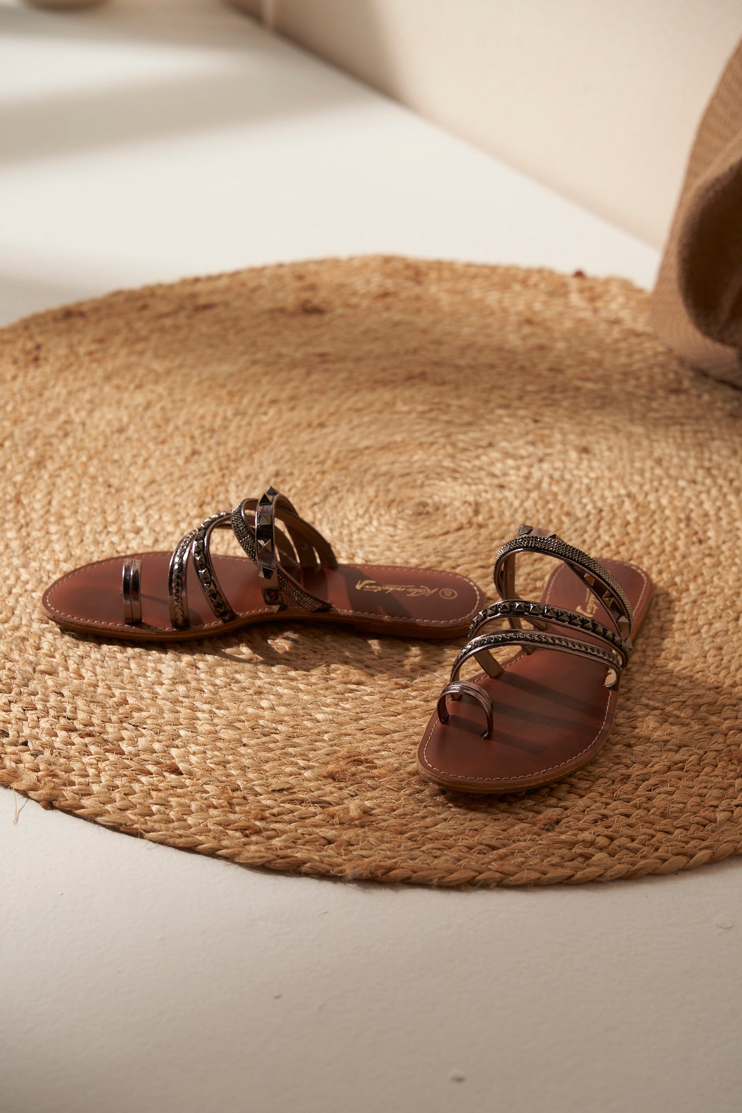 Pair of brown and silver sandals with decorative straps on a woven mat