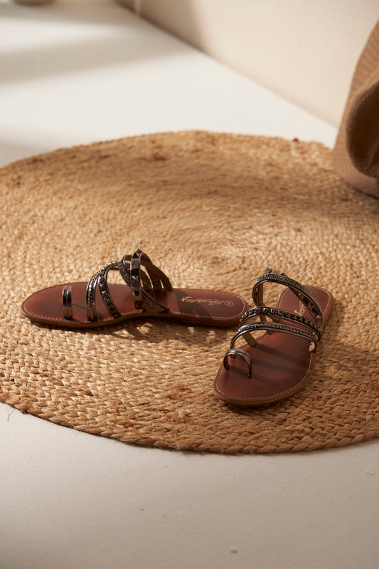 Pair of brown and silver sandals with decorative straps on a woven mat