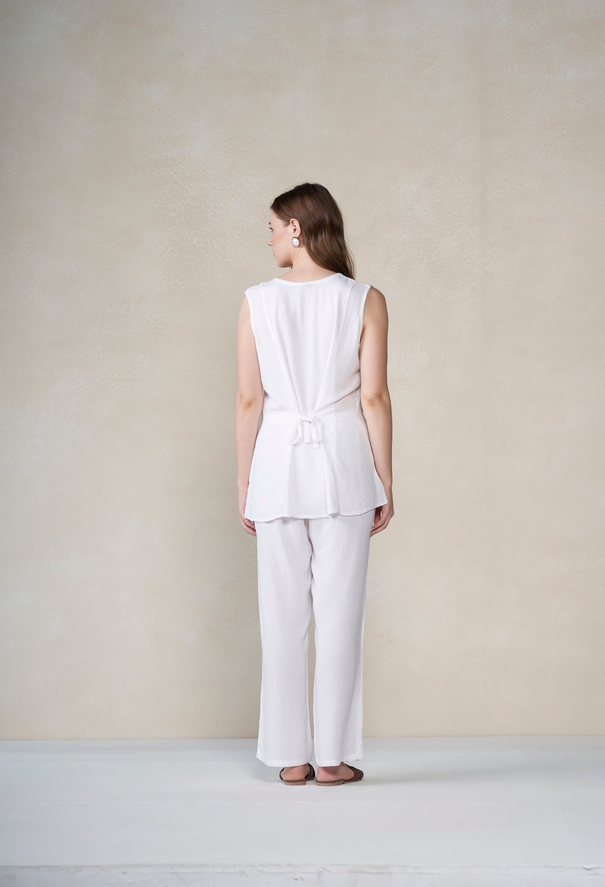 Person wearing a white sleeveless top and pants against a plain background