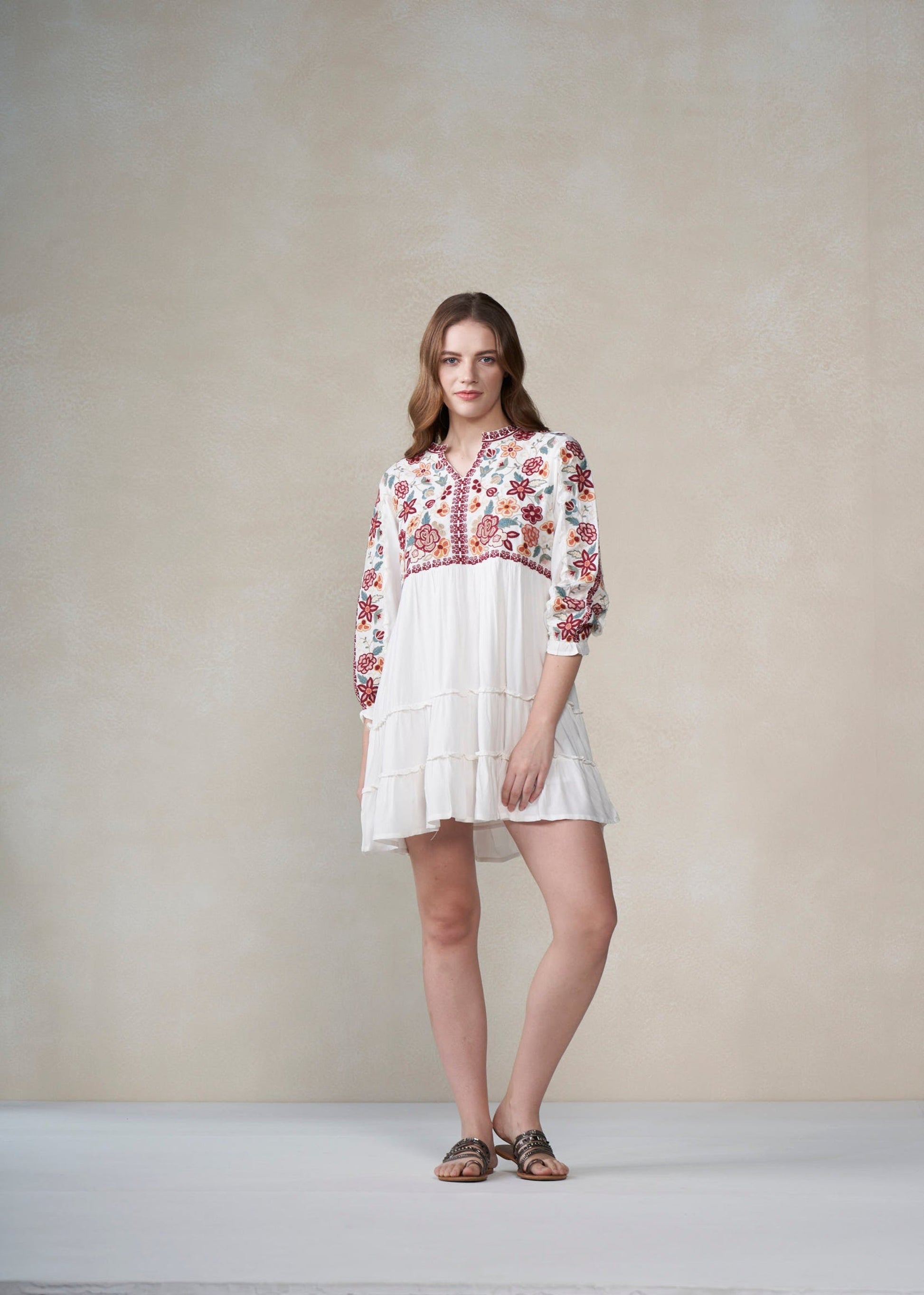 Woman wearing a white dress with floral embroidery against a plain background