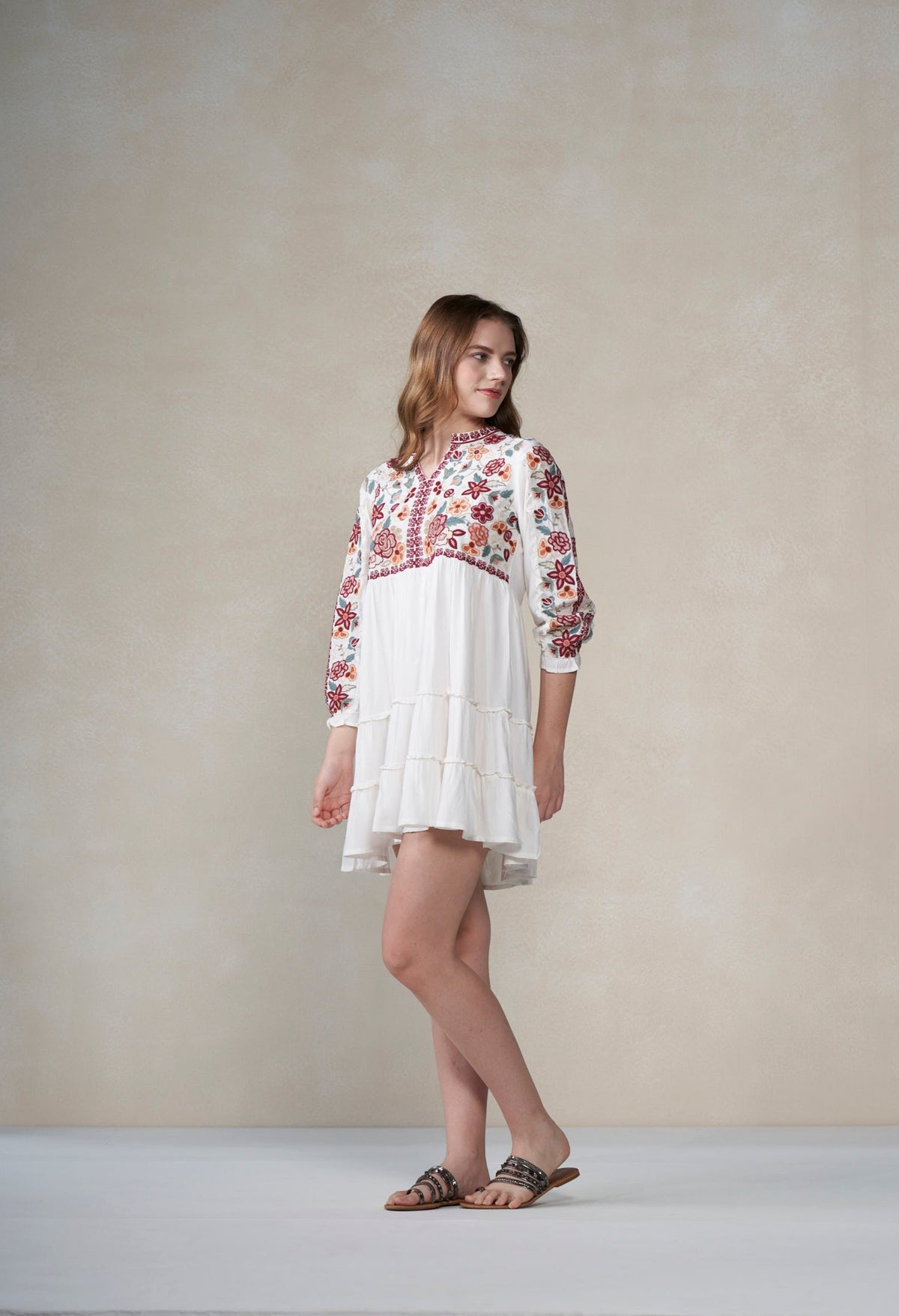 Woman wearing a white dress with floral embroidery against a plain background