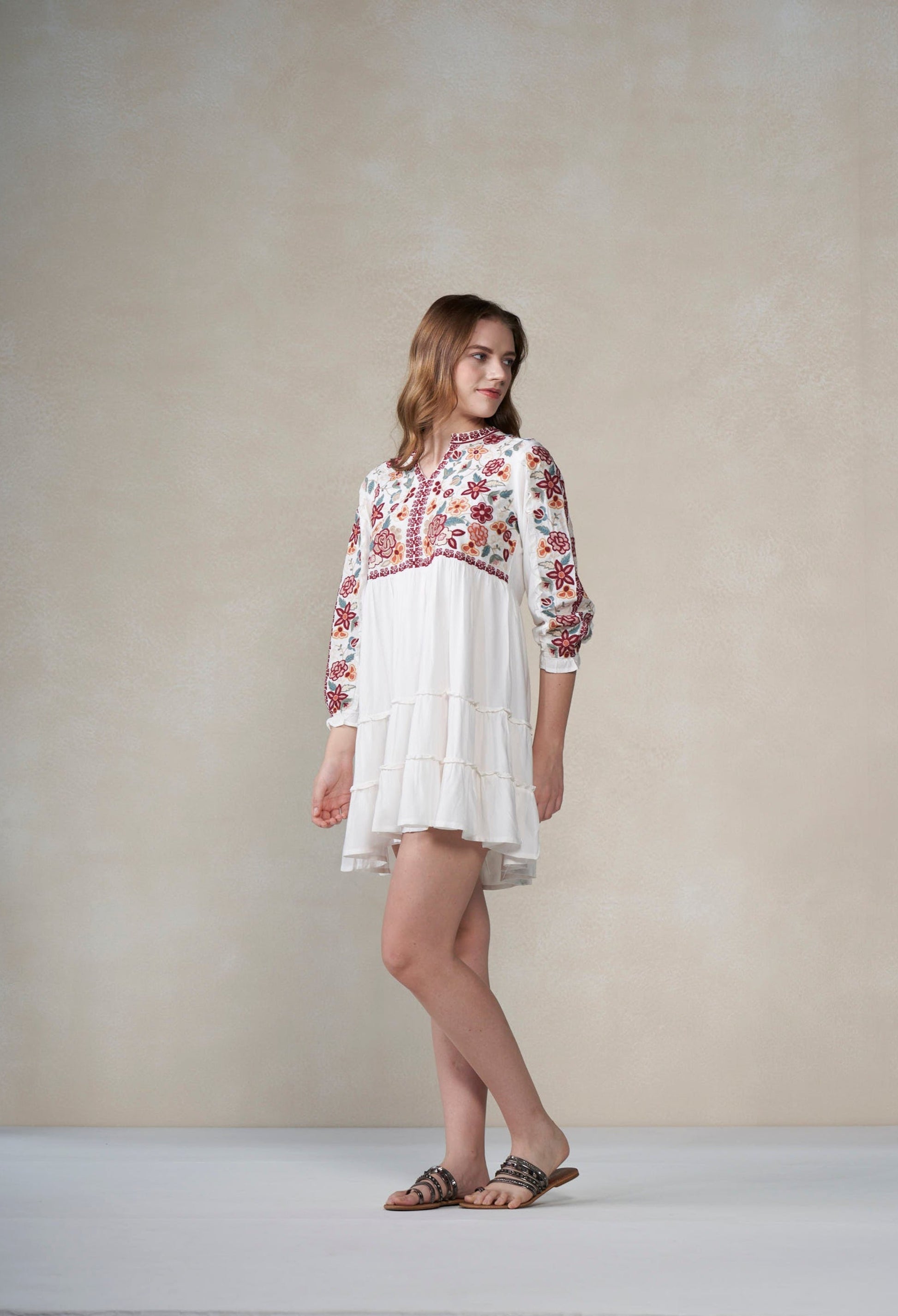 Woman wearing a white dress with floral embroidery against a plain background