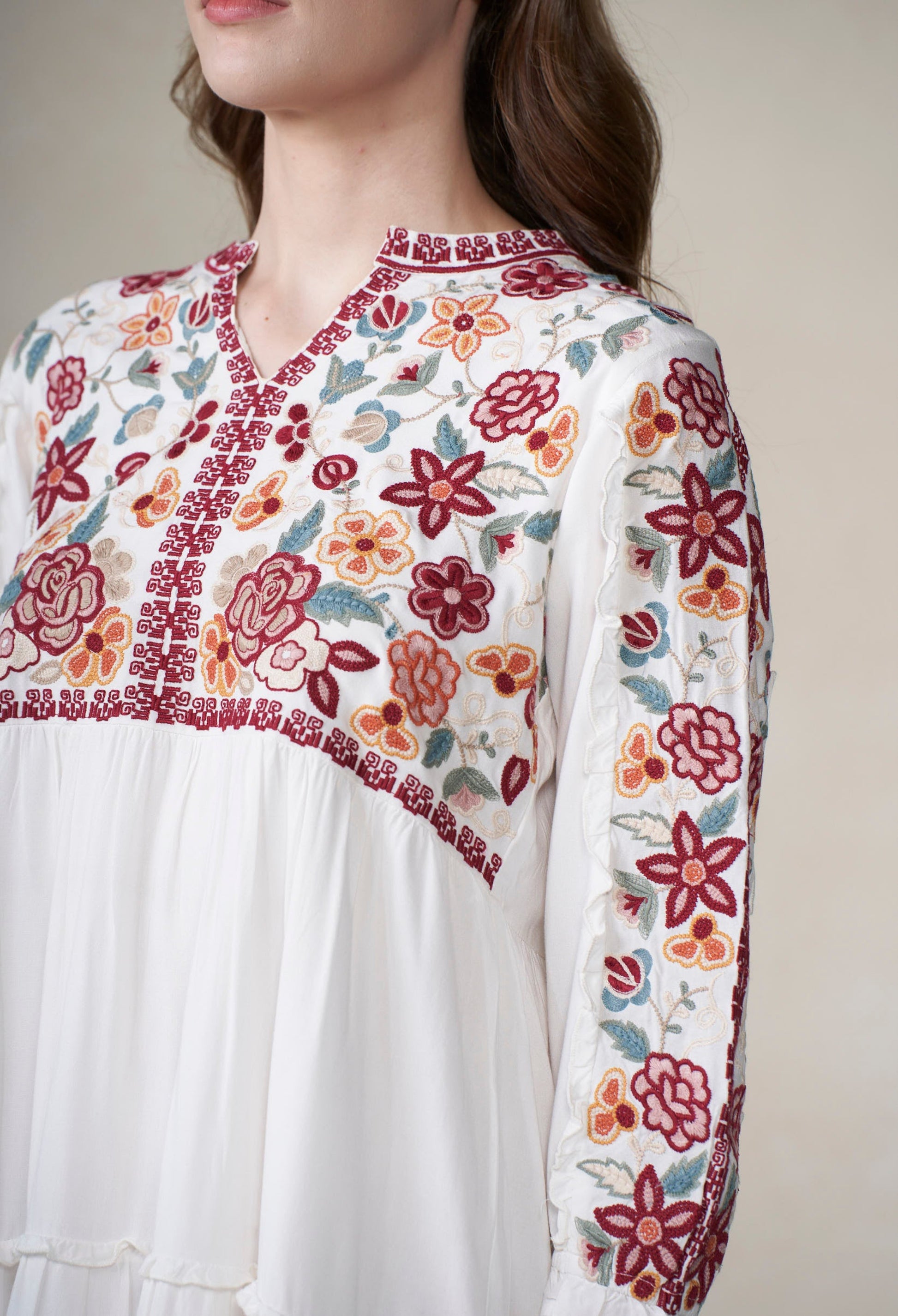 Woman wearing a white dress with floral embroidery against a plain background