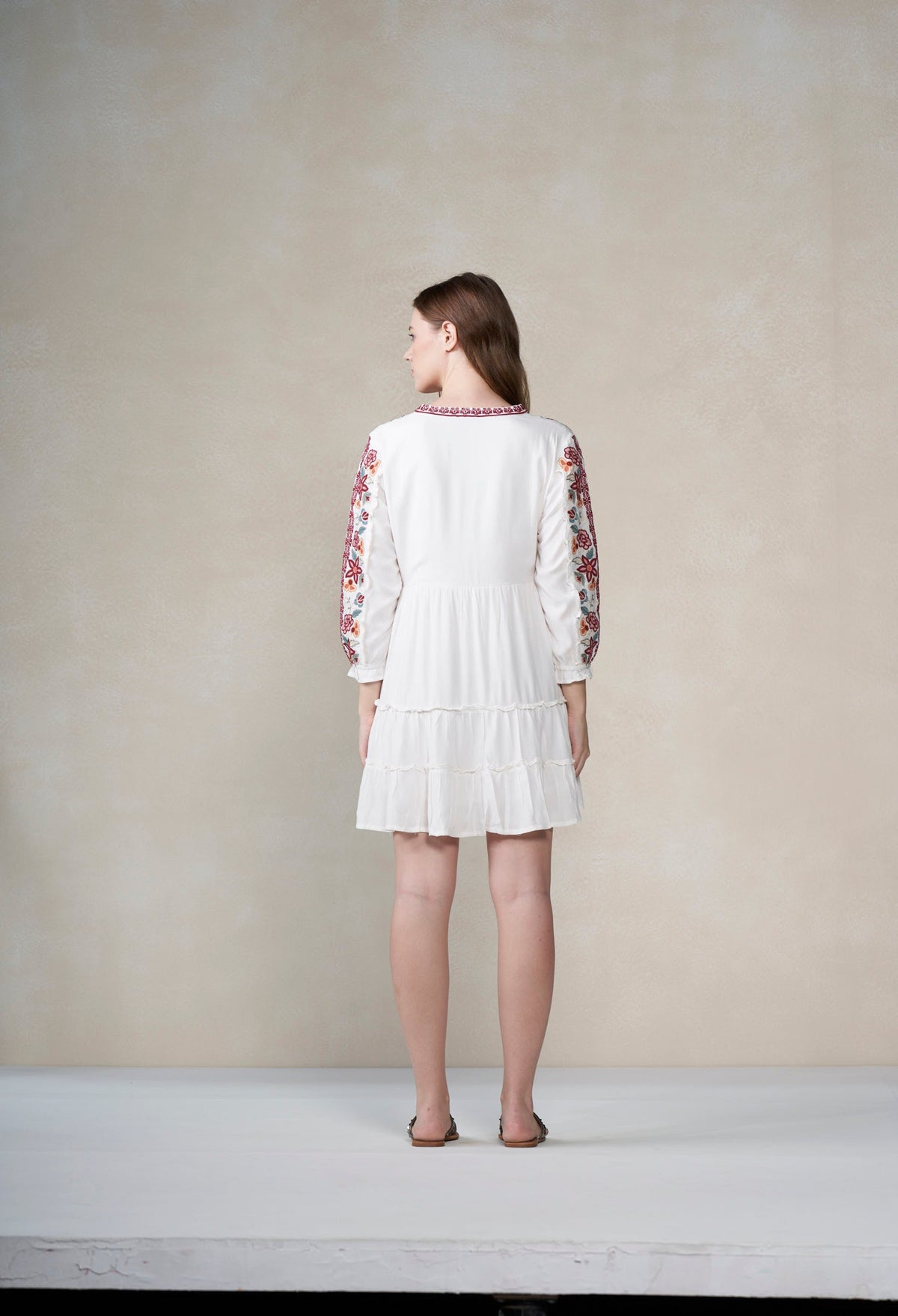 Woman wearing a white dress with floral sleeves against a plain background