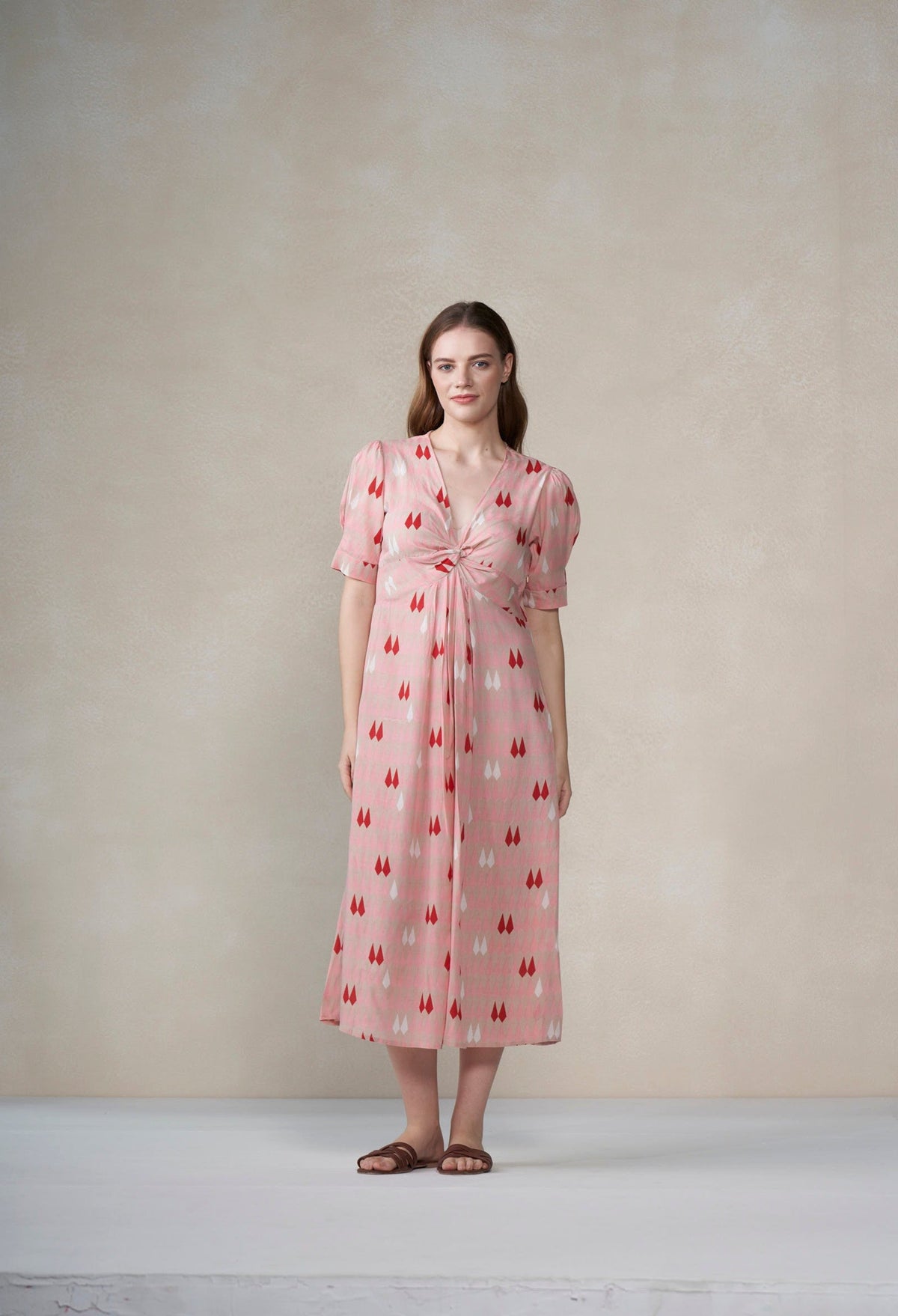 Woman wearing a pink dress with a pattern against a plain background