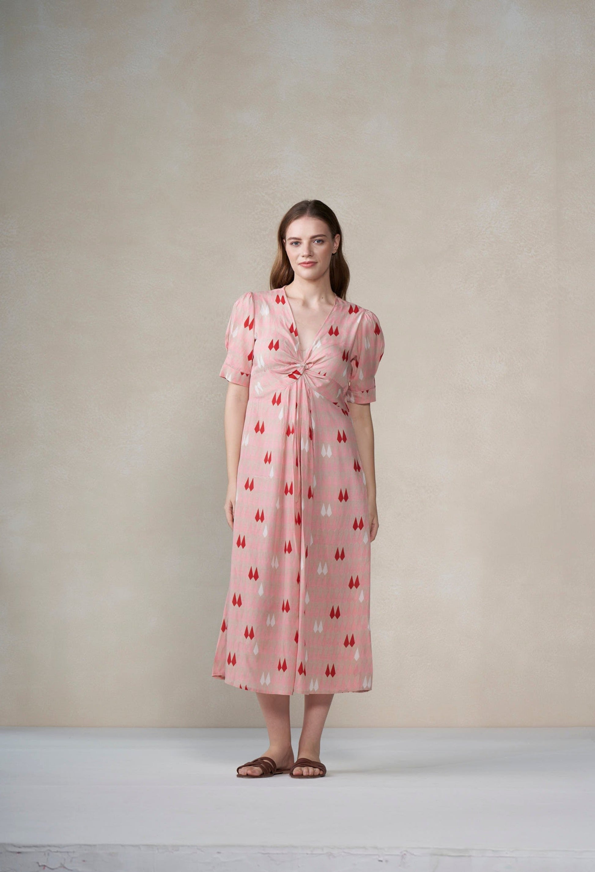 Woman wearing a pink dress with a pattern against a plain background