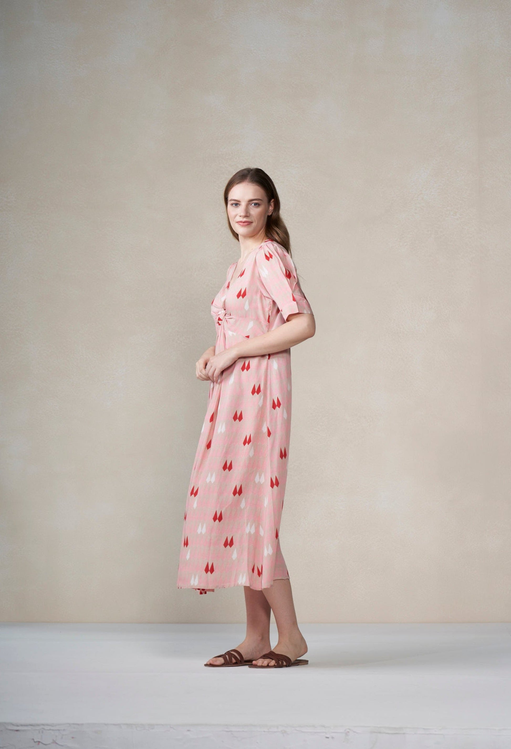 Woman wearing a pink dress with a pattern against a plain background