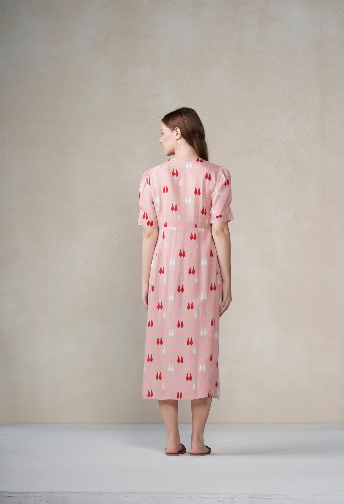 Woman wearing a pink dress with a red pattern against a plain background