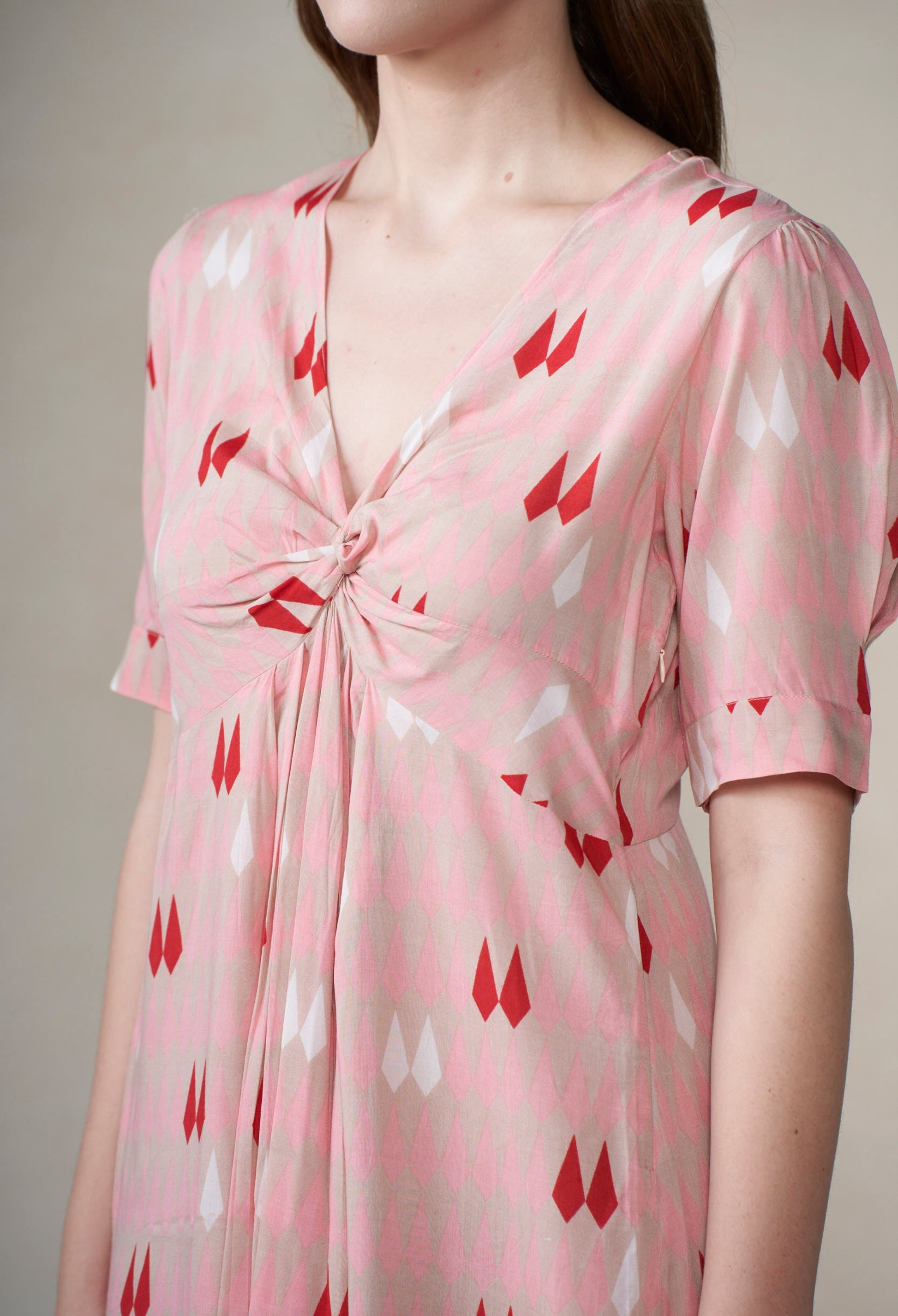 Pink dress with red pattern worn by a person against a neutral background