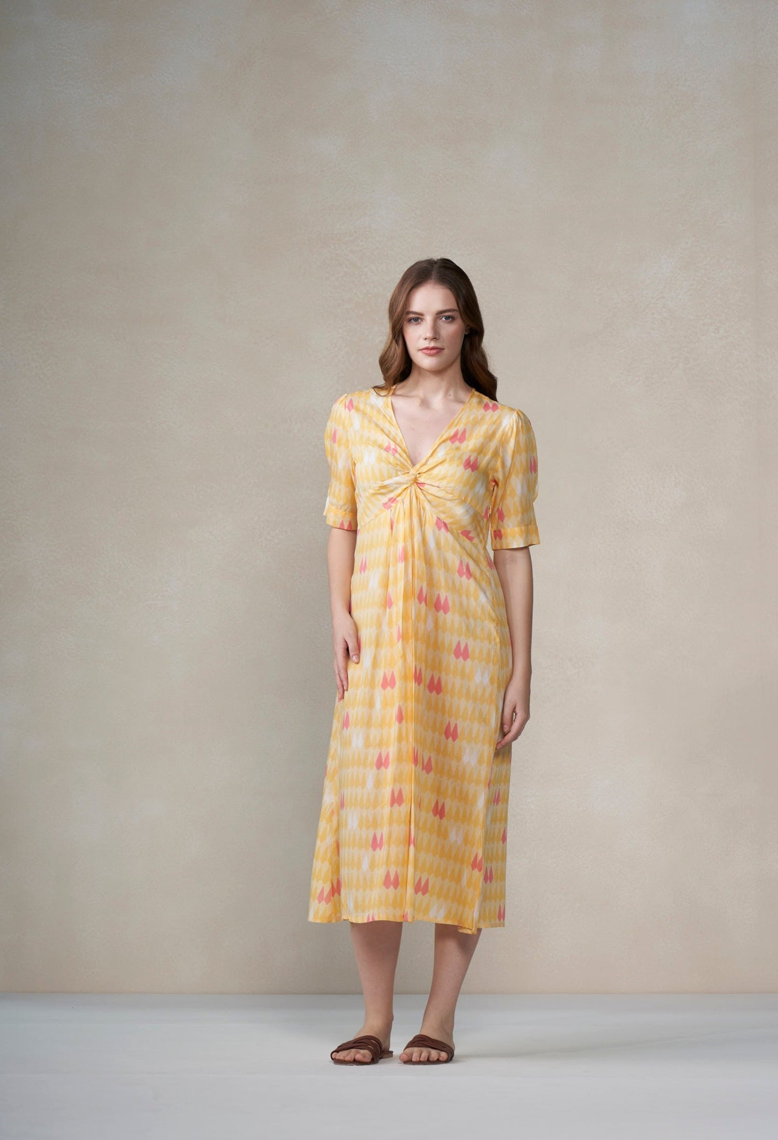 Woman wearing a yellow patterned dress against a plain background
