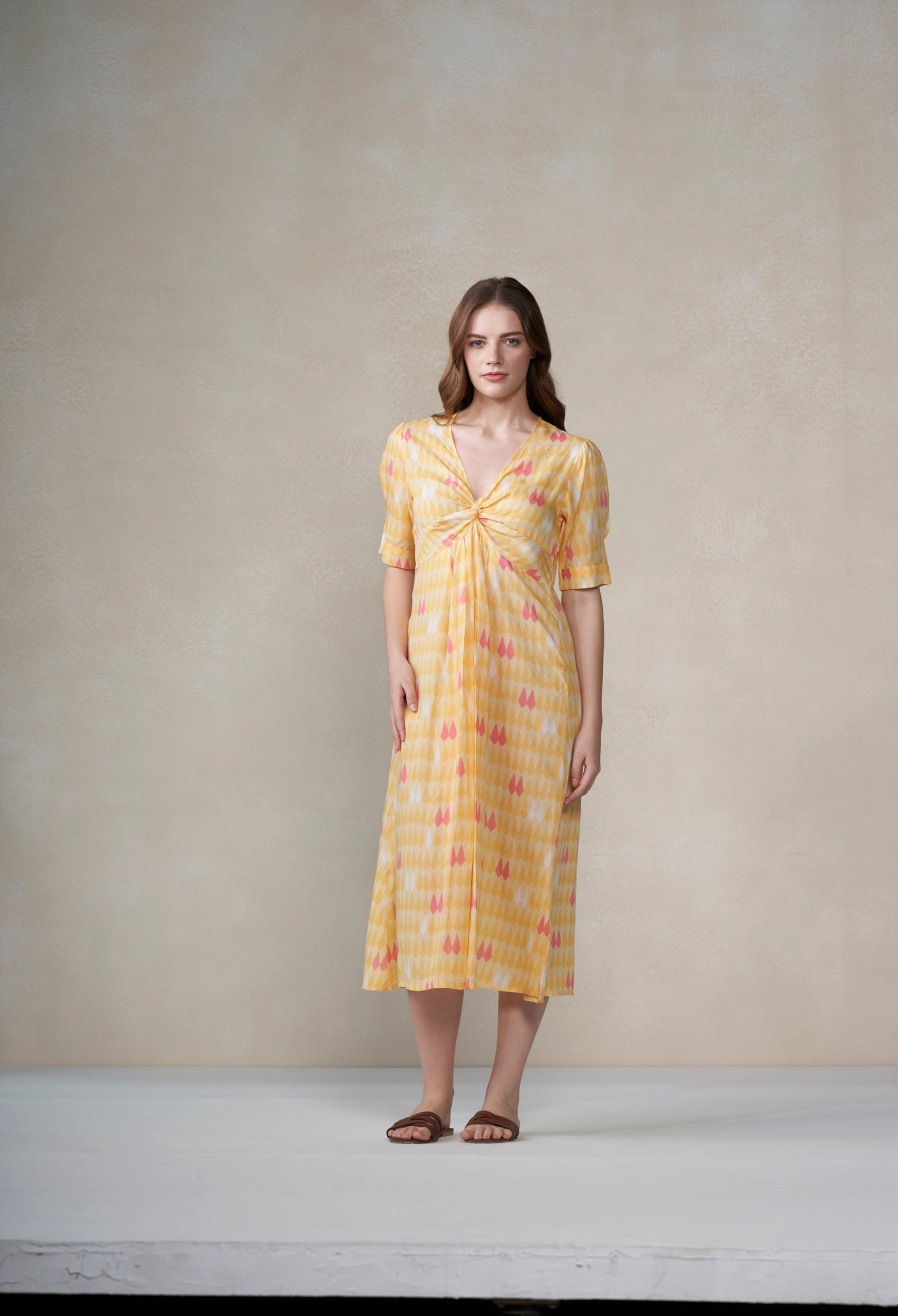 Woman wearing a yellow patterned dress against a plain background