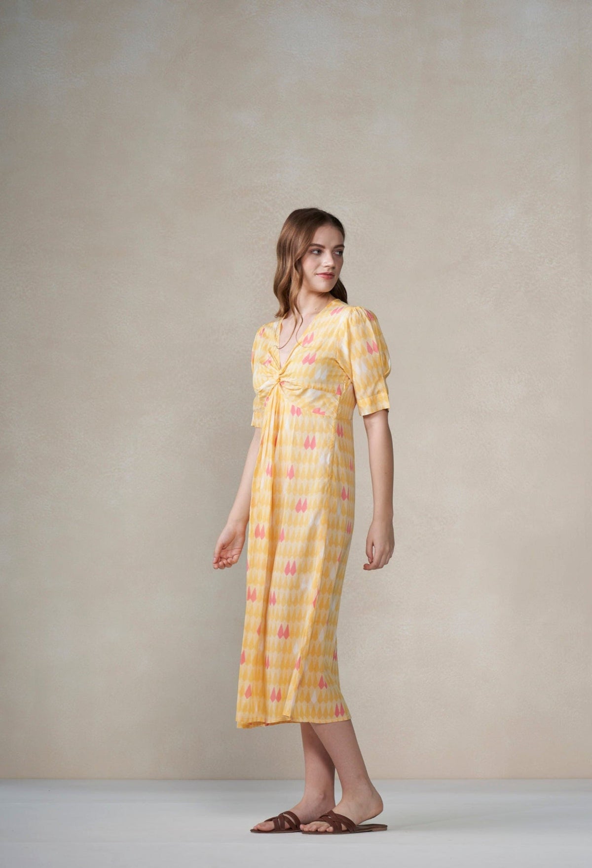 Woman wearing a yellow dress with a pattern against a plain background