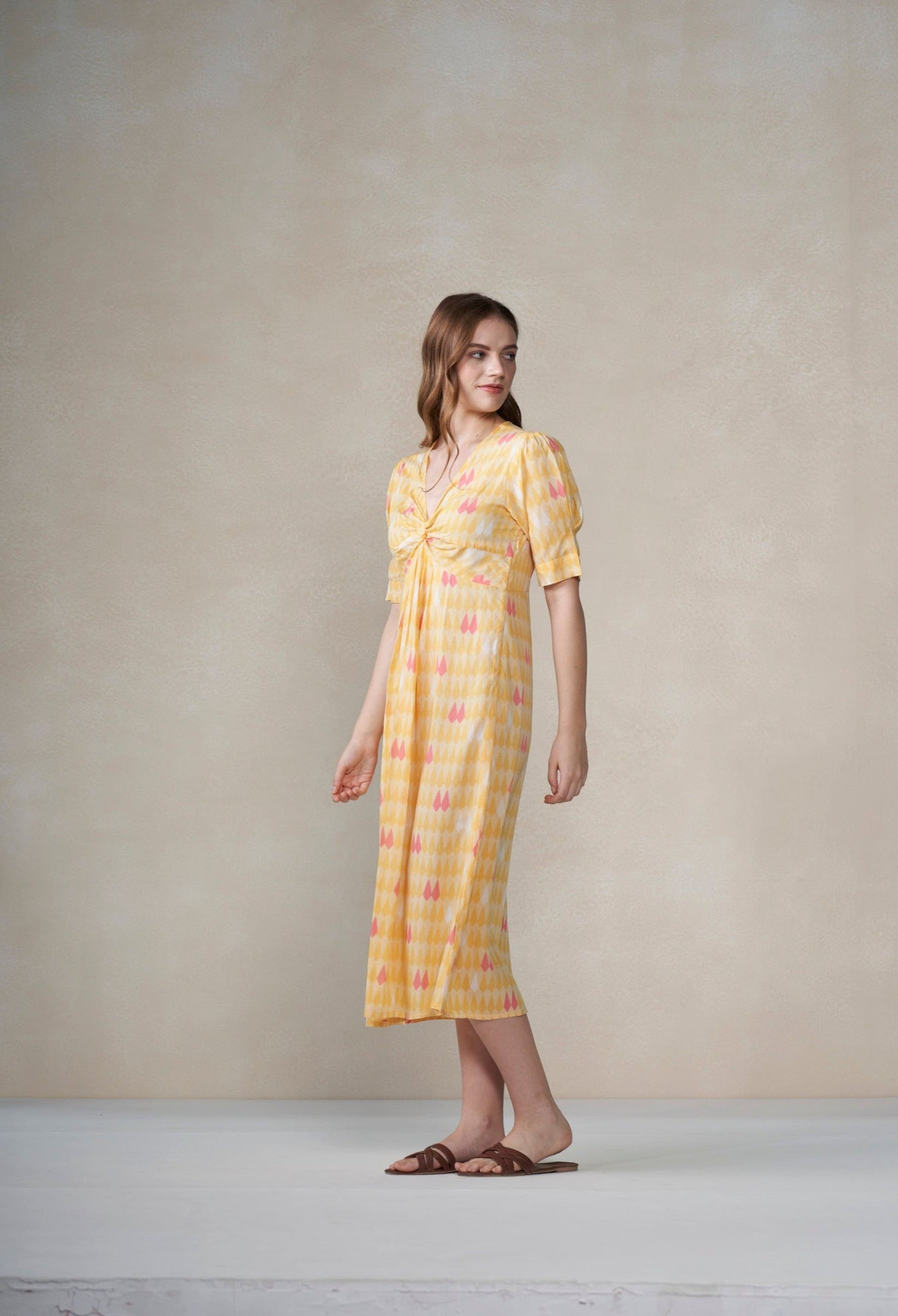 Woman wearing a yellow dress with a pattern against a plain background