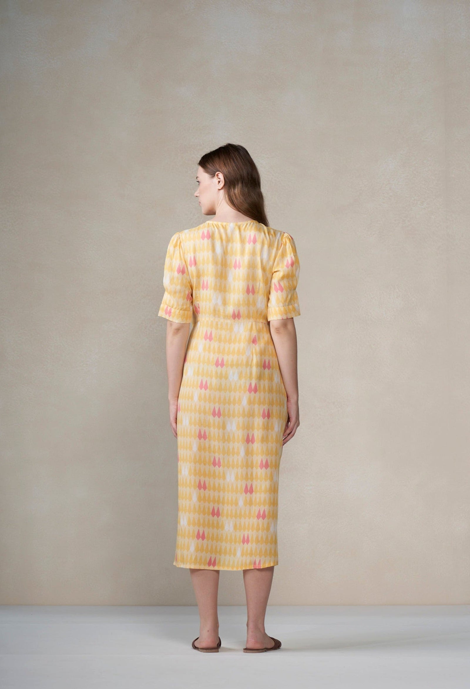 Woman wearing a yellow dress with a subtle pattern against a plain background
