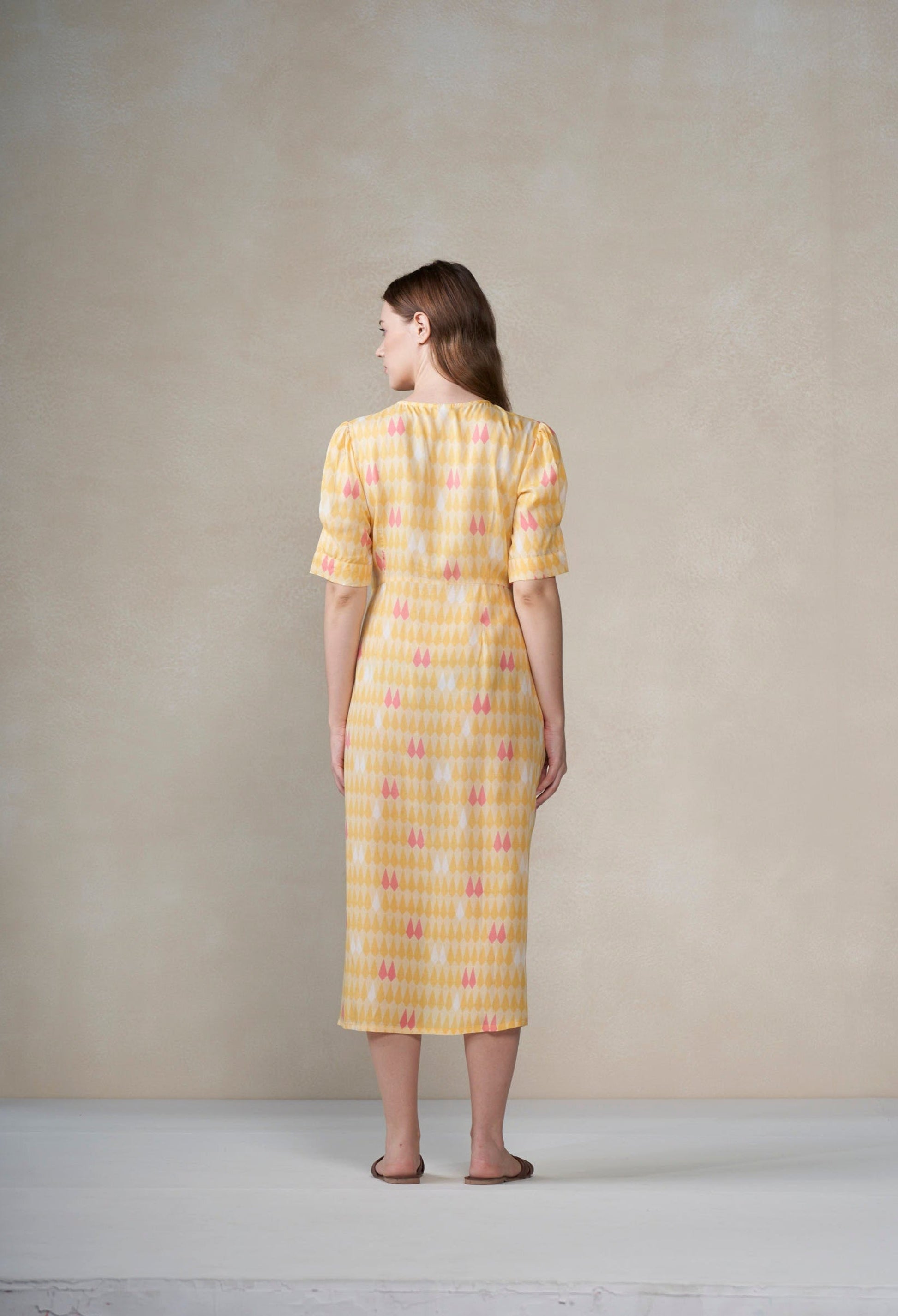 Woman wearing a yellow dress with a subtle pattern against a plain background