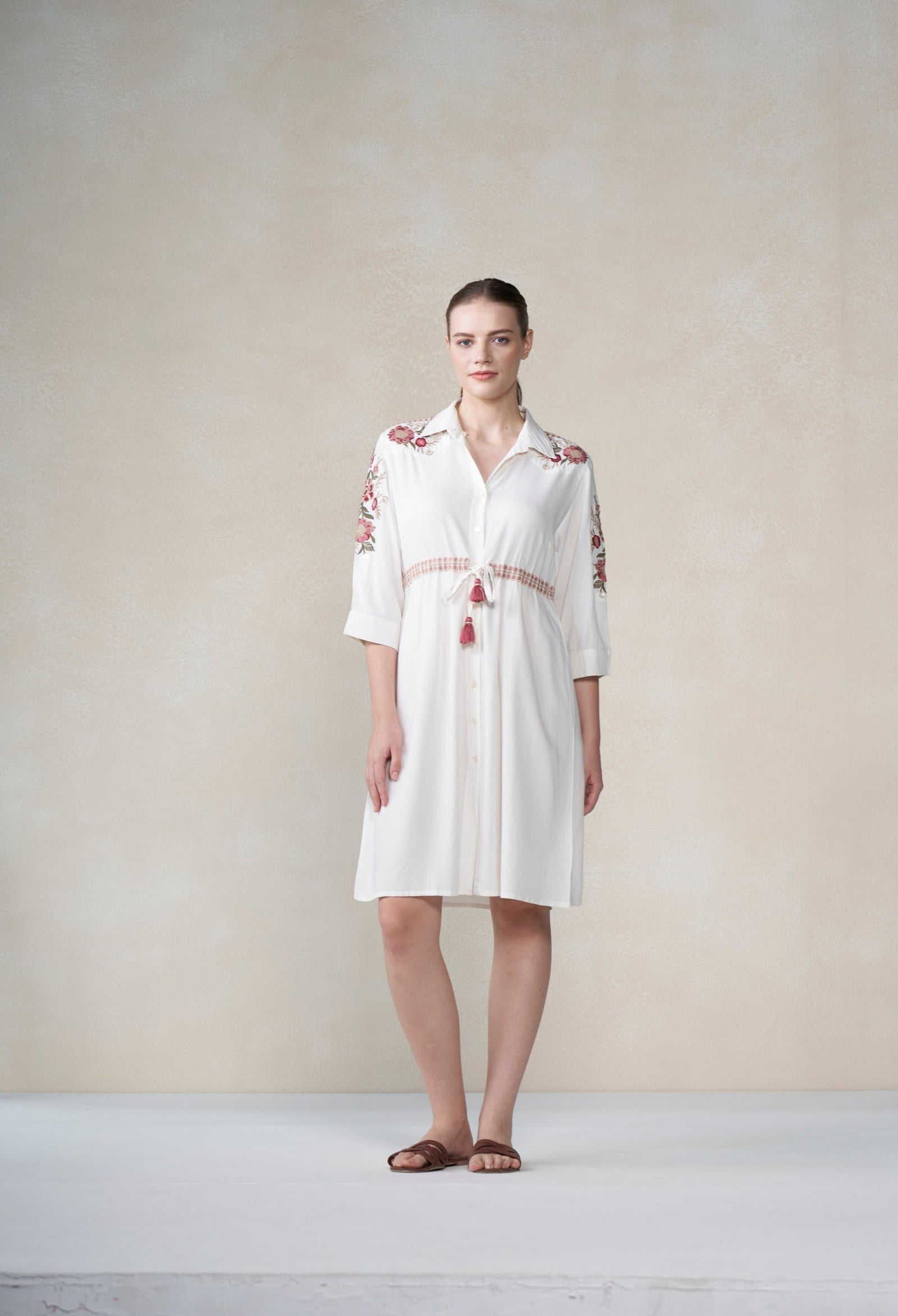 Woman wearing a white dress with red embroidery against a plain background