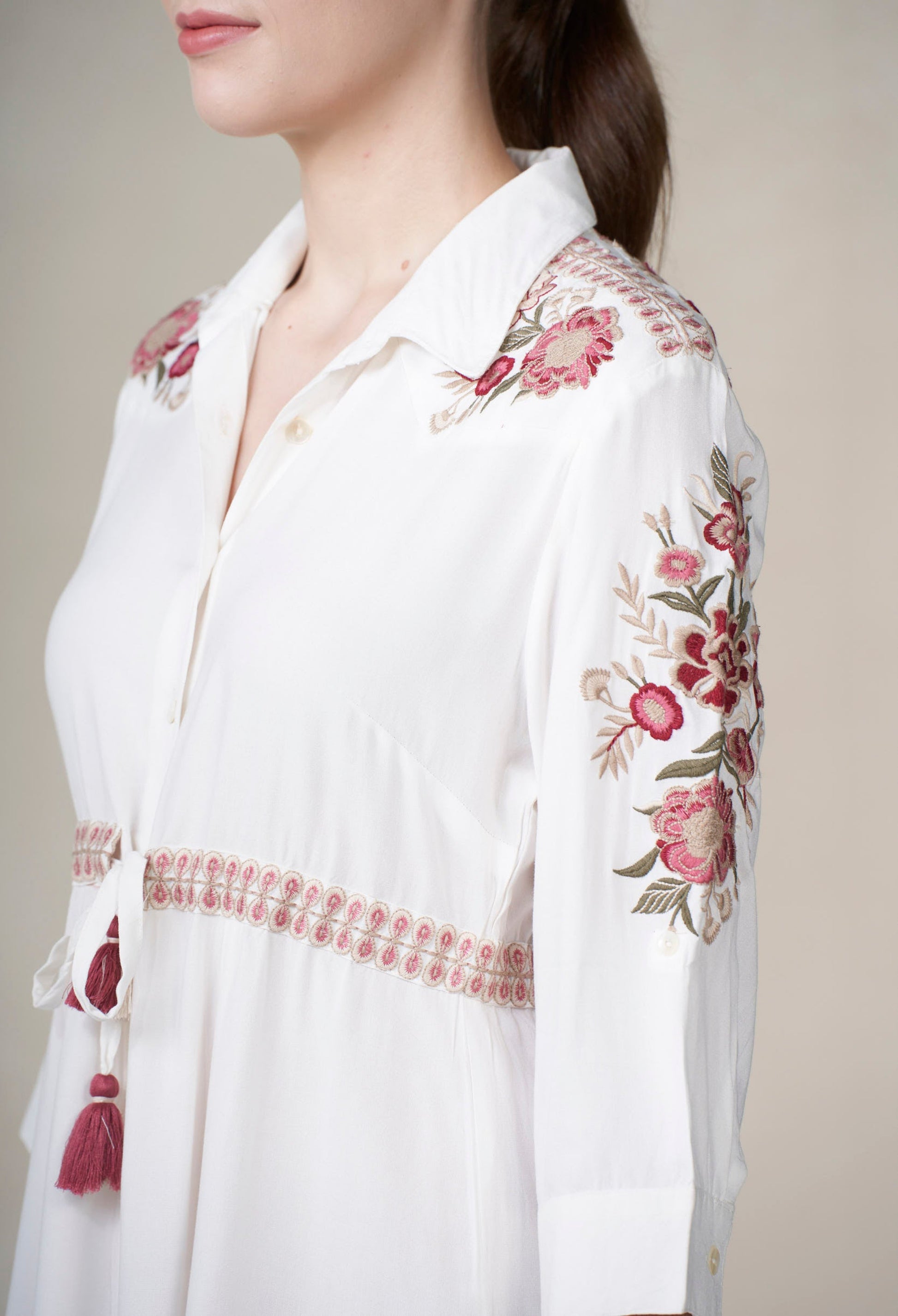 White blouse with floral embroidery and tassel details on a neutral background