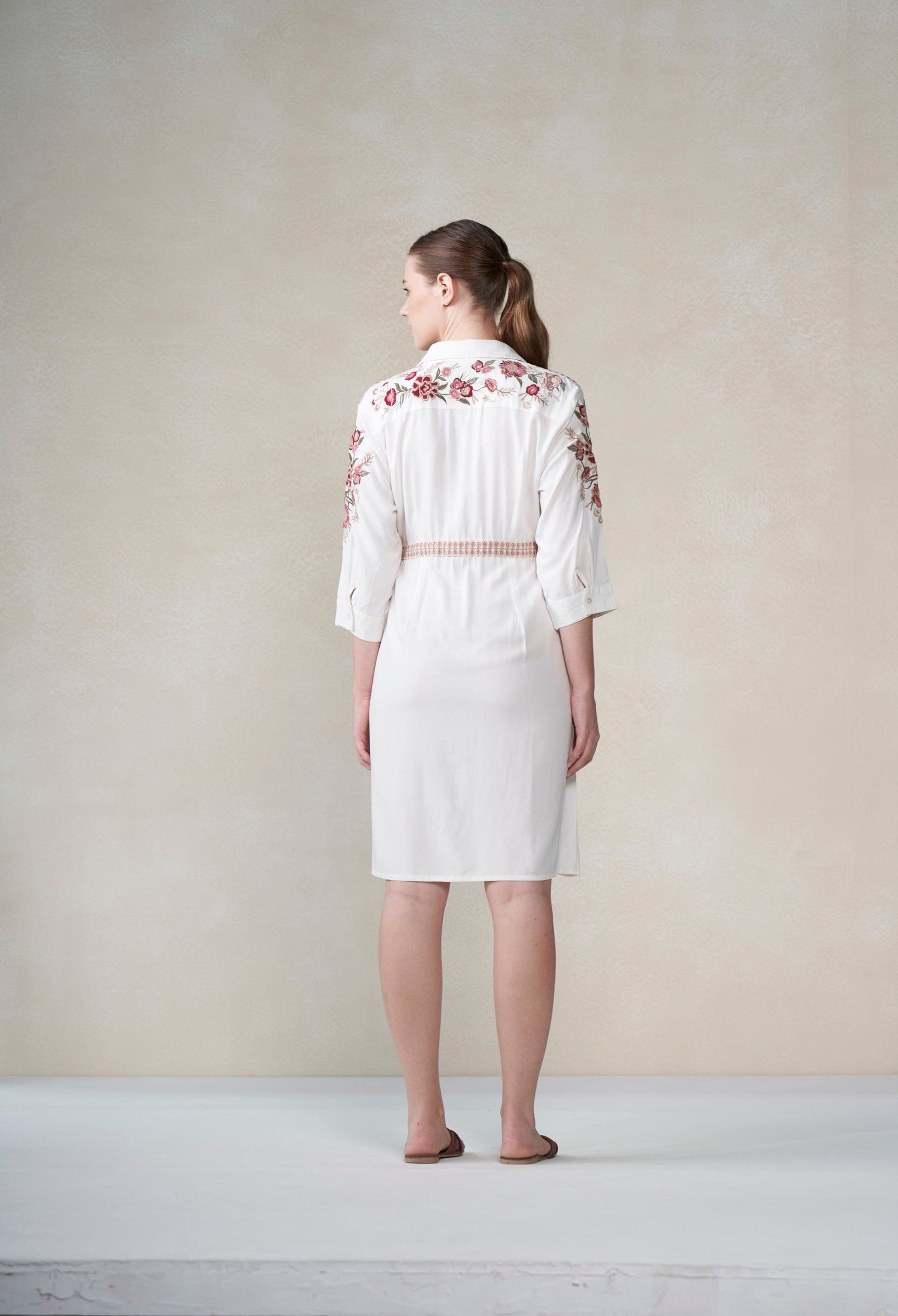 Woman wearing a white dress with floral embroidery on a plain background