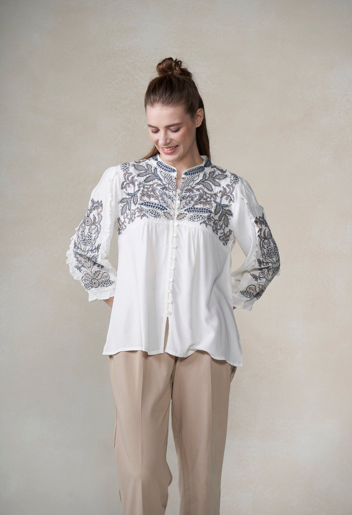 Woman wearing a white blouse with blue embroidery against a plain background