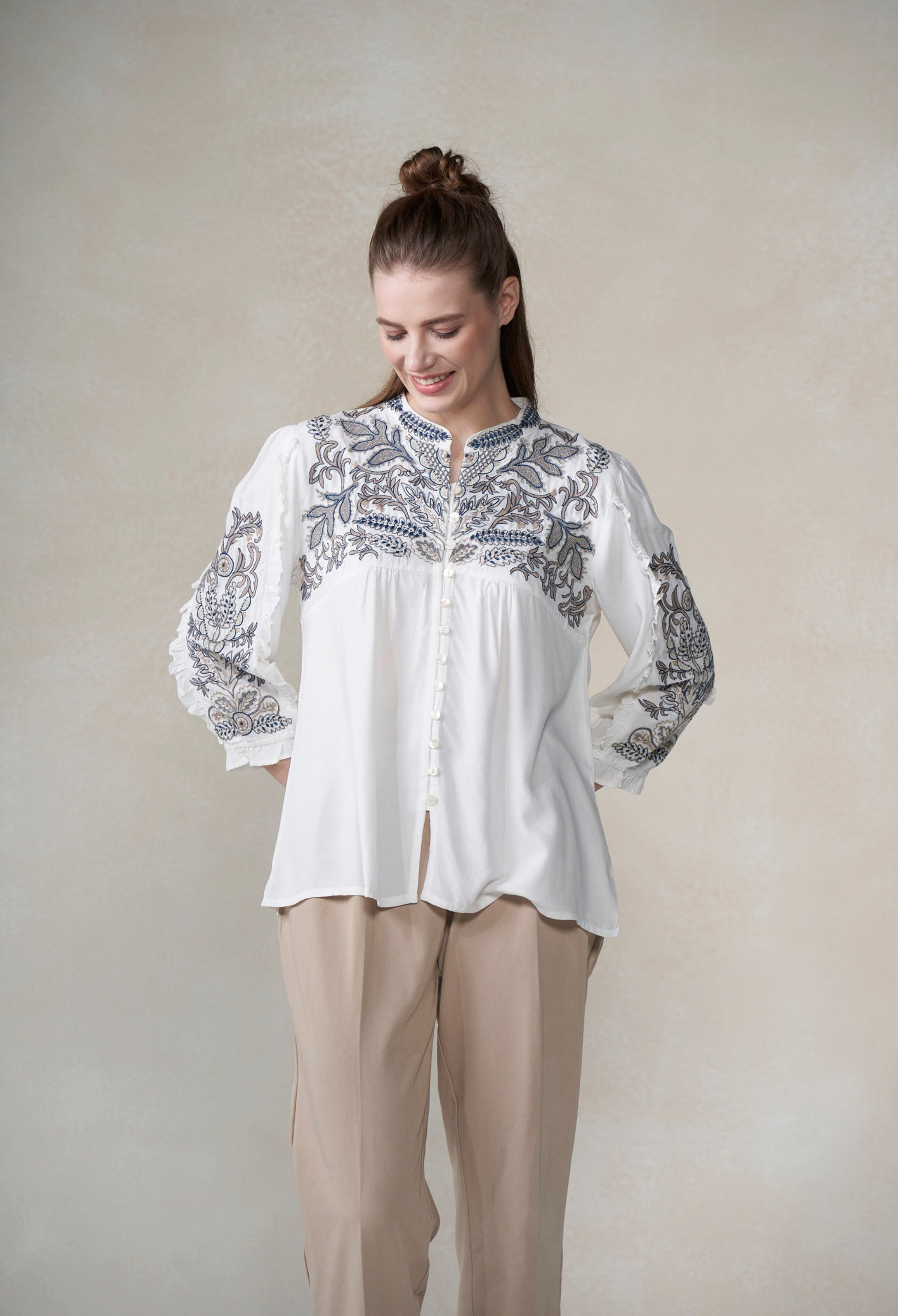 Woman wearing a white blouse with blue embroidery against a plain background