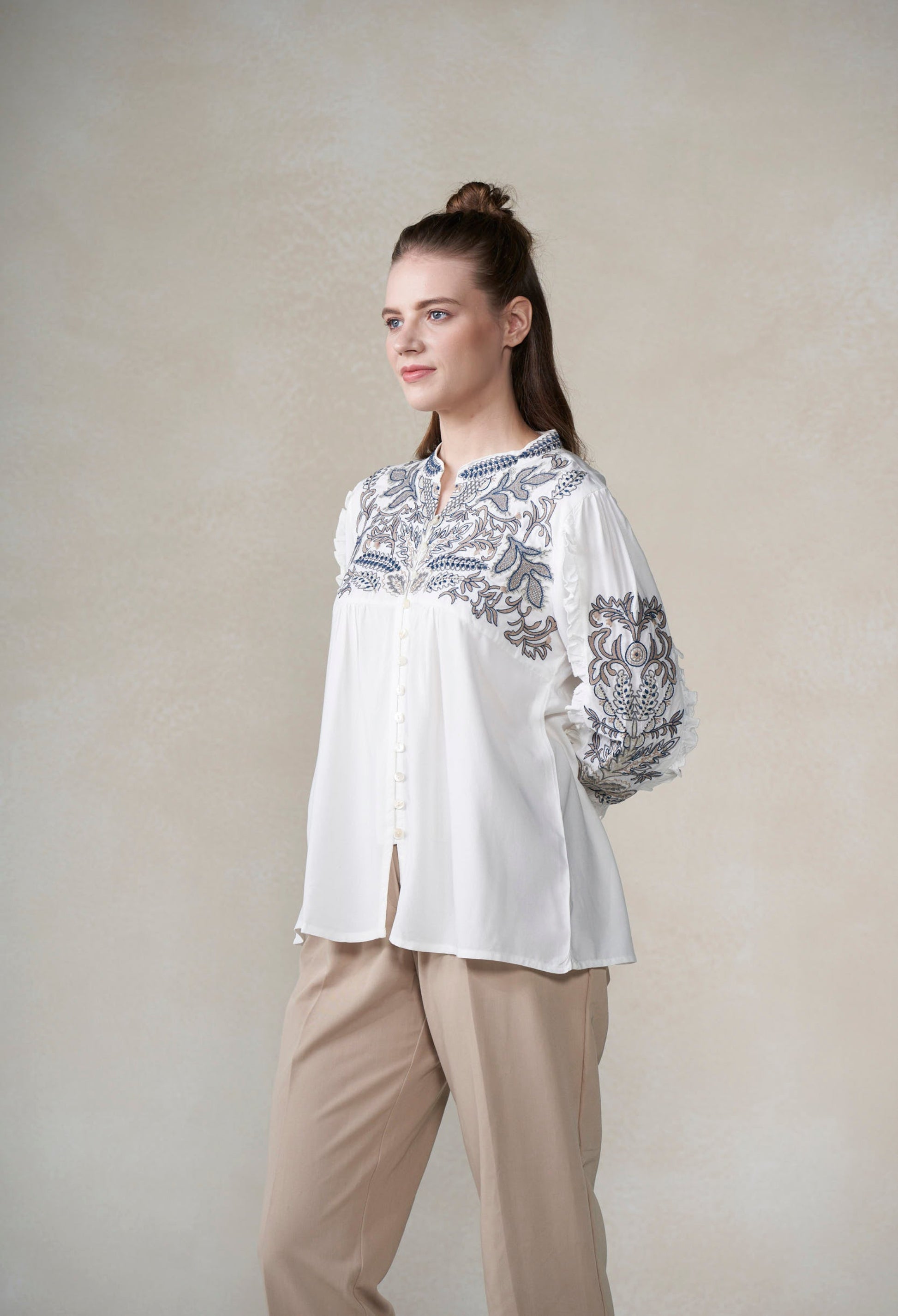 Woman wearing a white blouse with blue embroidery against a plain background