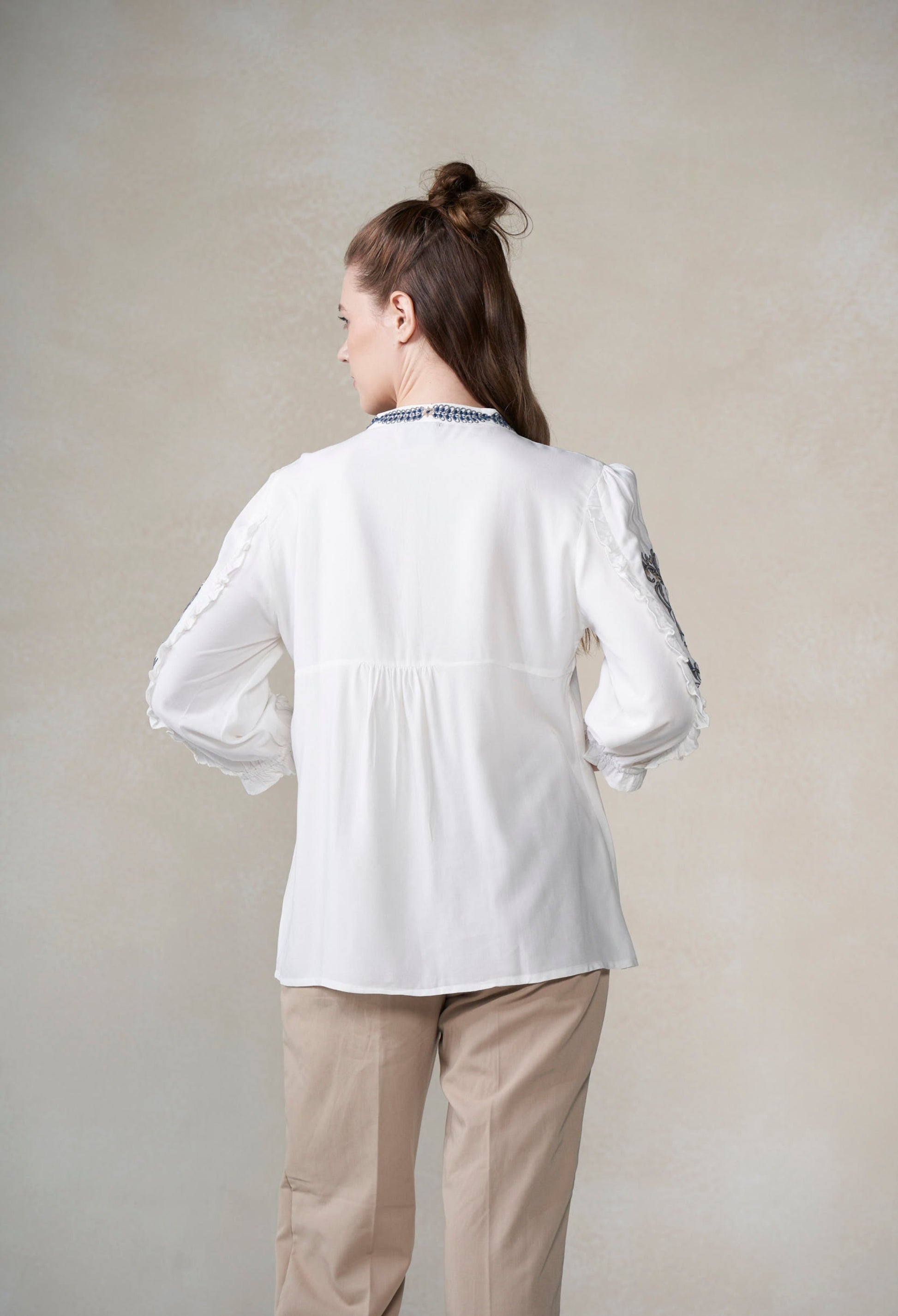 Woman wearing a white blouse with long sleeves and beige pants on a plain background