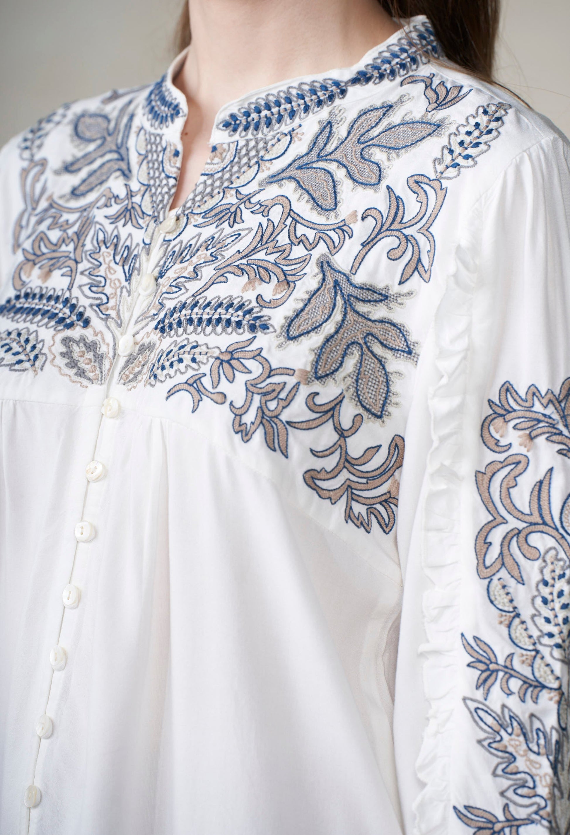 White shirt with blue floral embroidery on a plain background