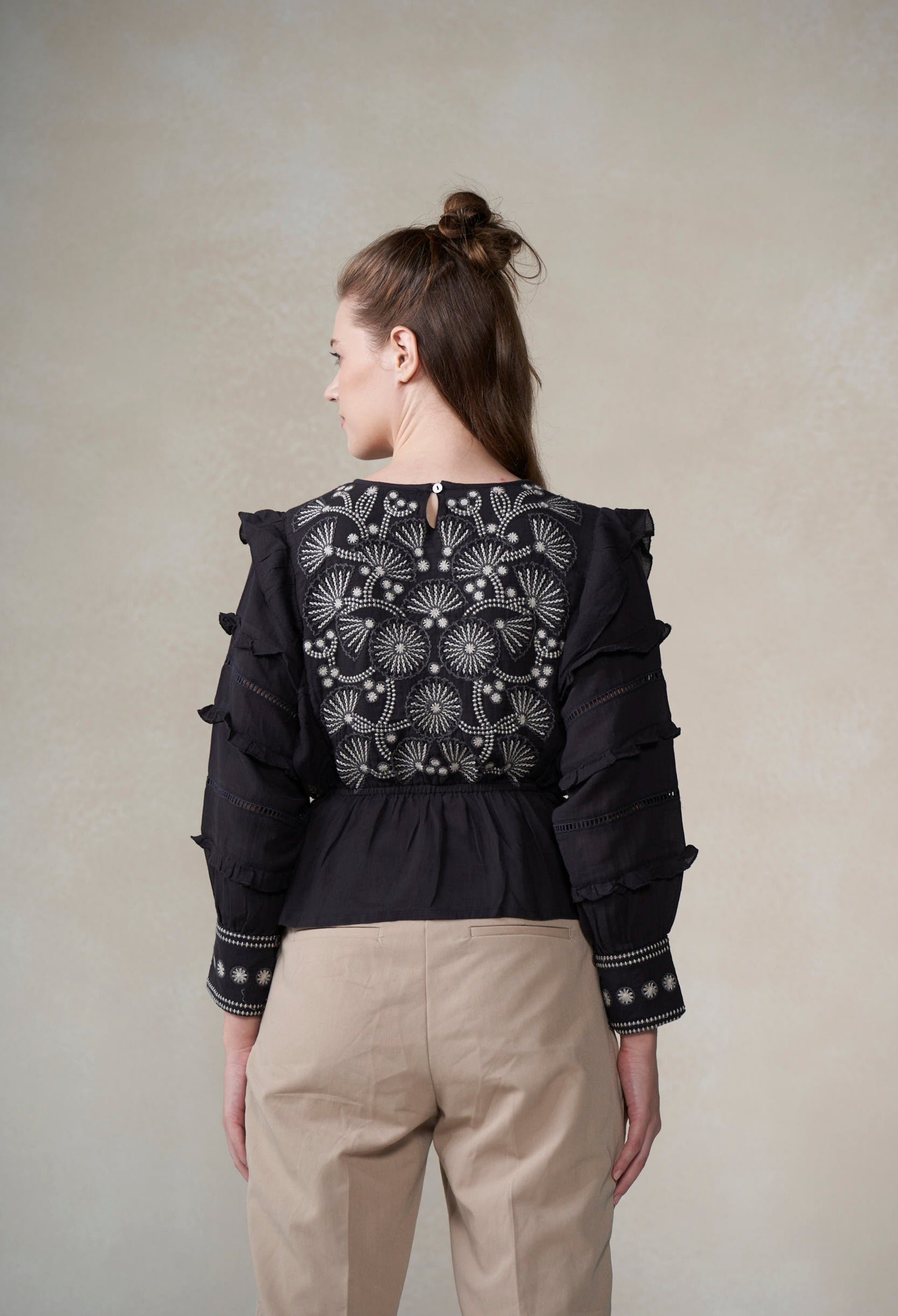 Woman wearing a black embroidered blouse with ruffled sleeves on a beige background