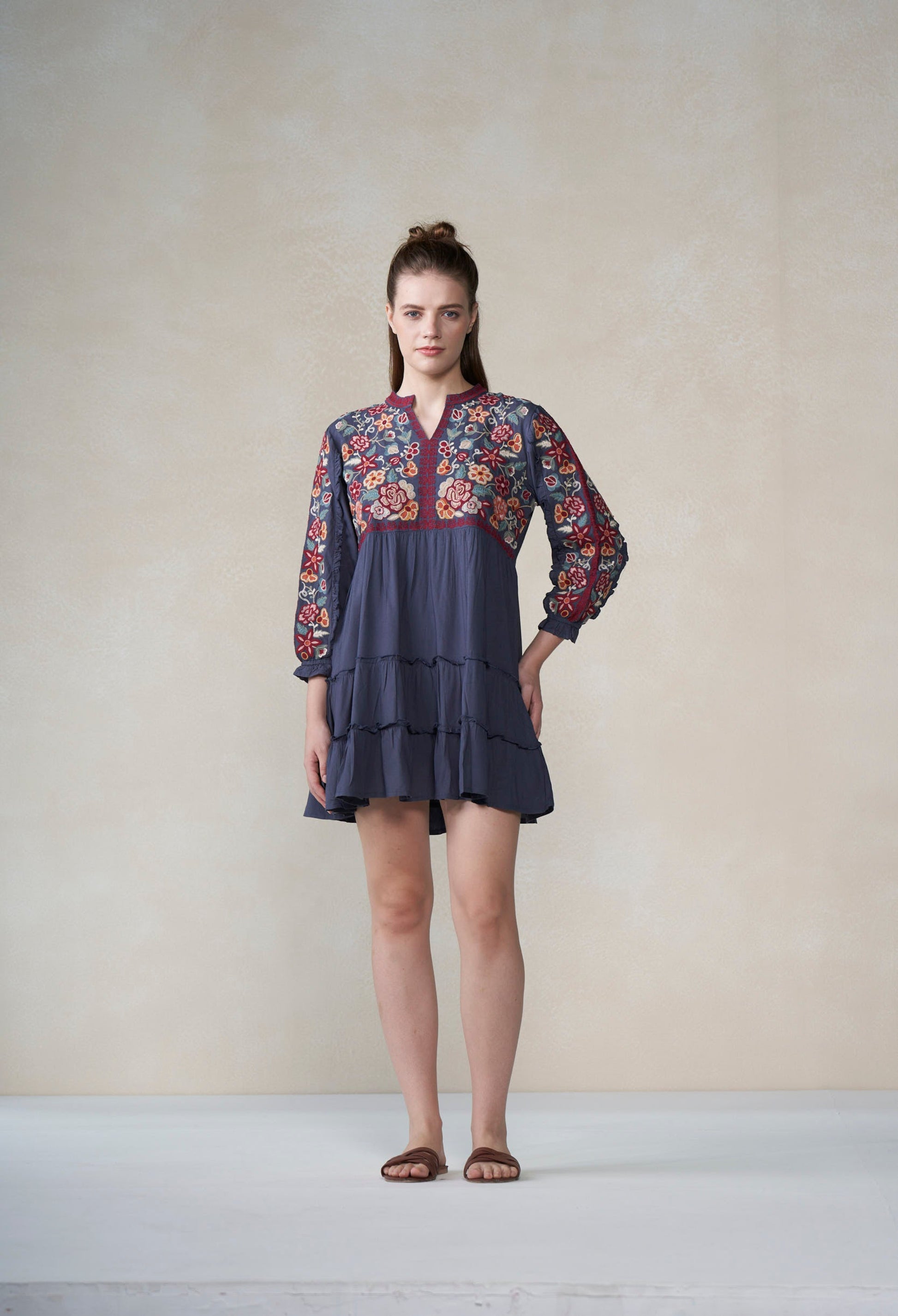 Woman wearing a dark blue dress with floral embroidery against a plain background