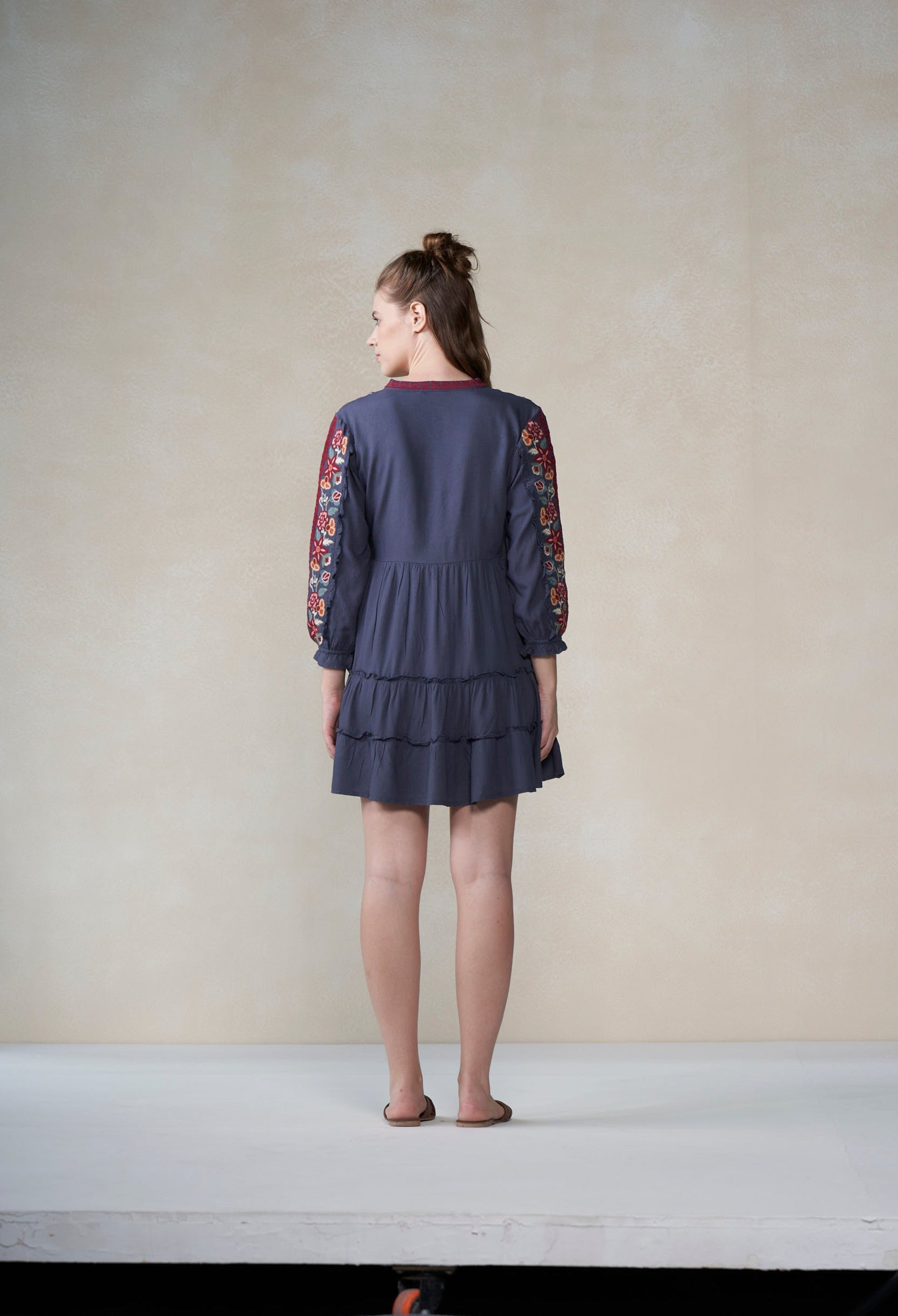 Woman wearing a dark blue dress with floral sleeves against a plain background