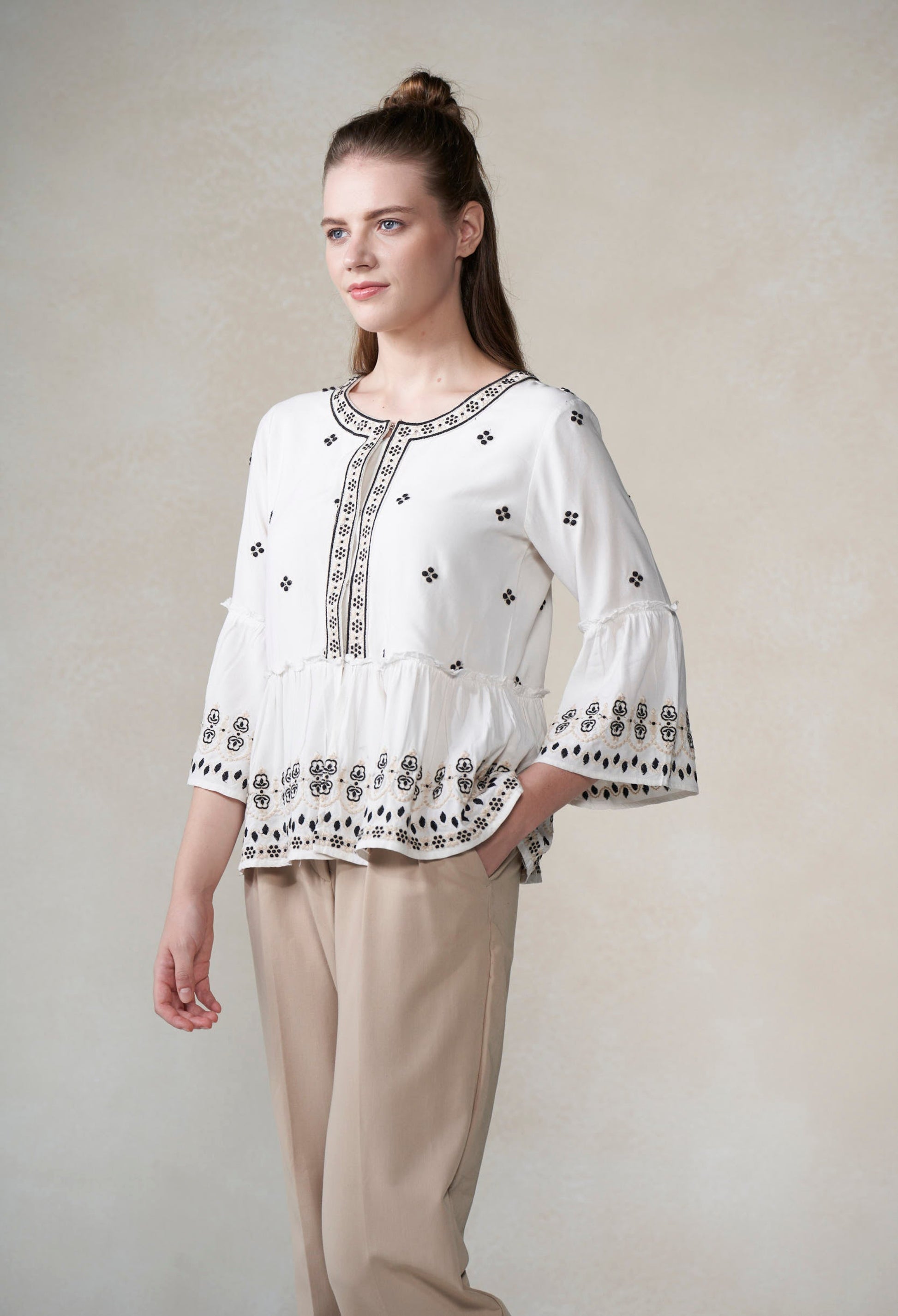 Woman wearing a white blouse with black embroidery on a plain background